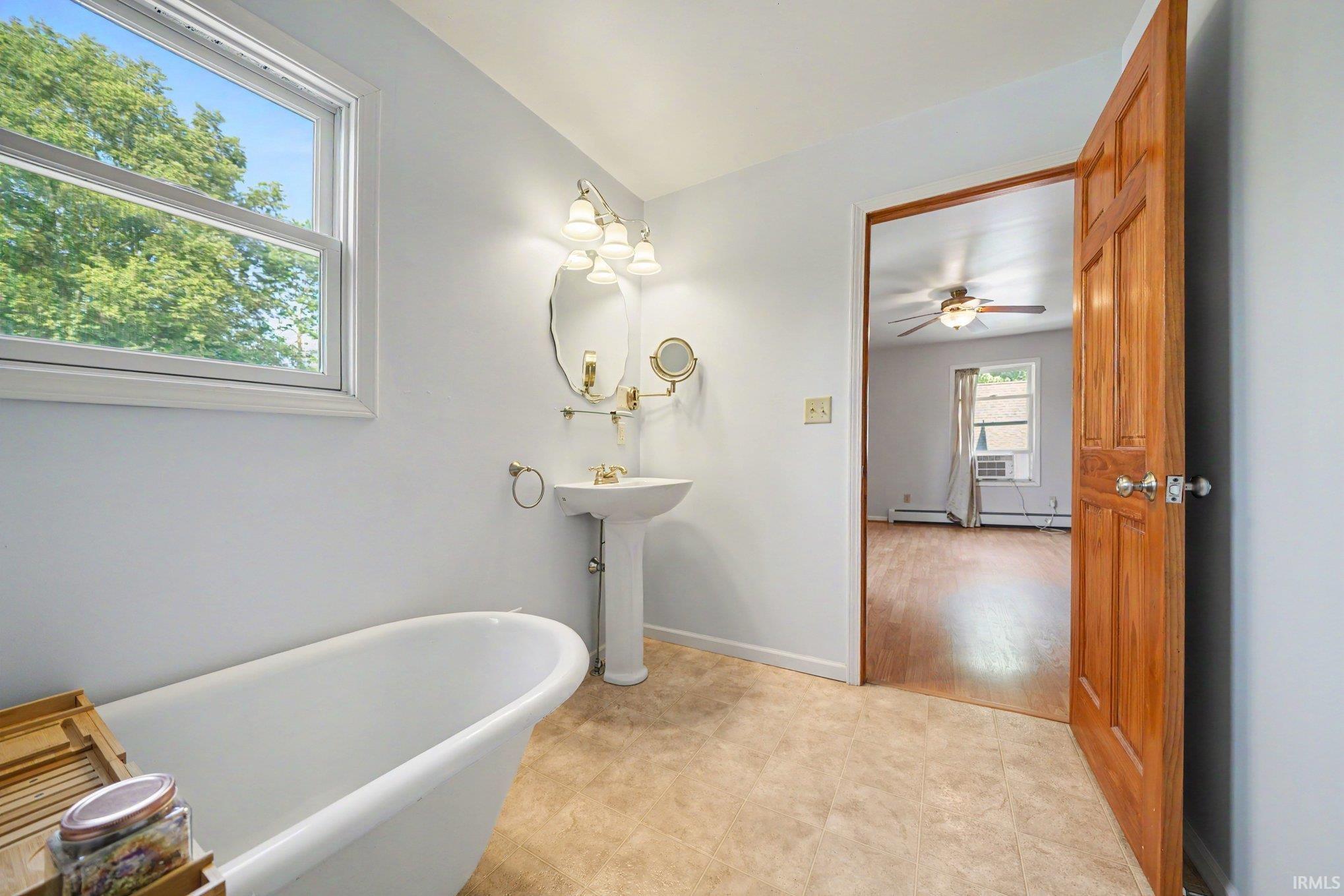 Bathroom featuring a white clawfoot tub, pedestal sink with brass fixtures, and a vanity light with a decorative mirror
