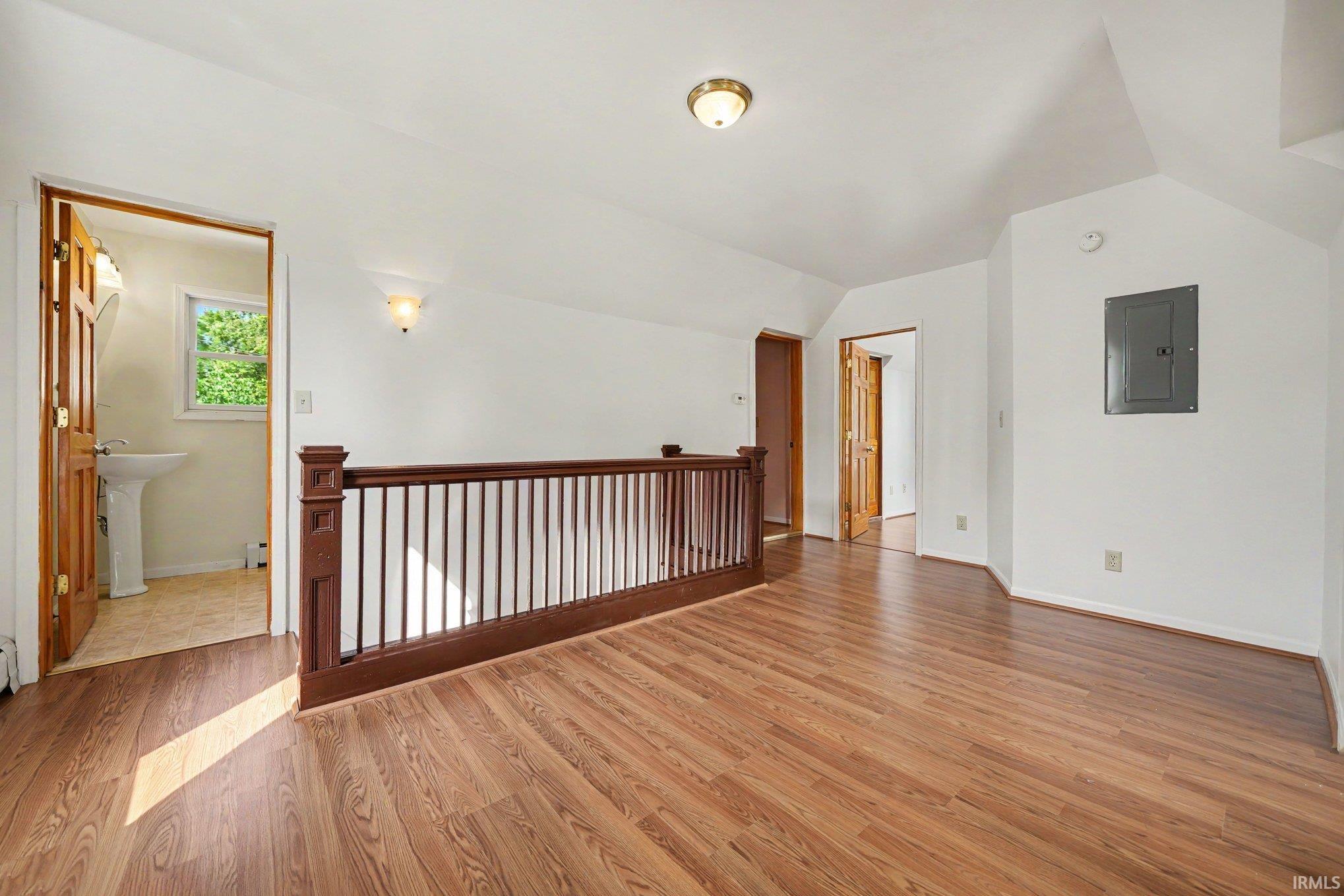 Spacious upper-level landing featuring wood-finish flooring, a dark wood railing, multiple doorways, and a flush-mount ceiling light
