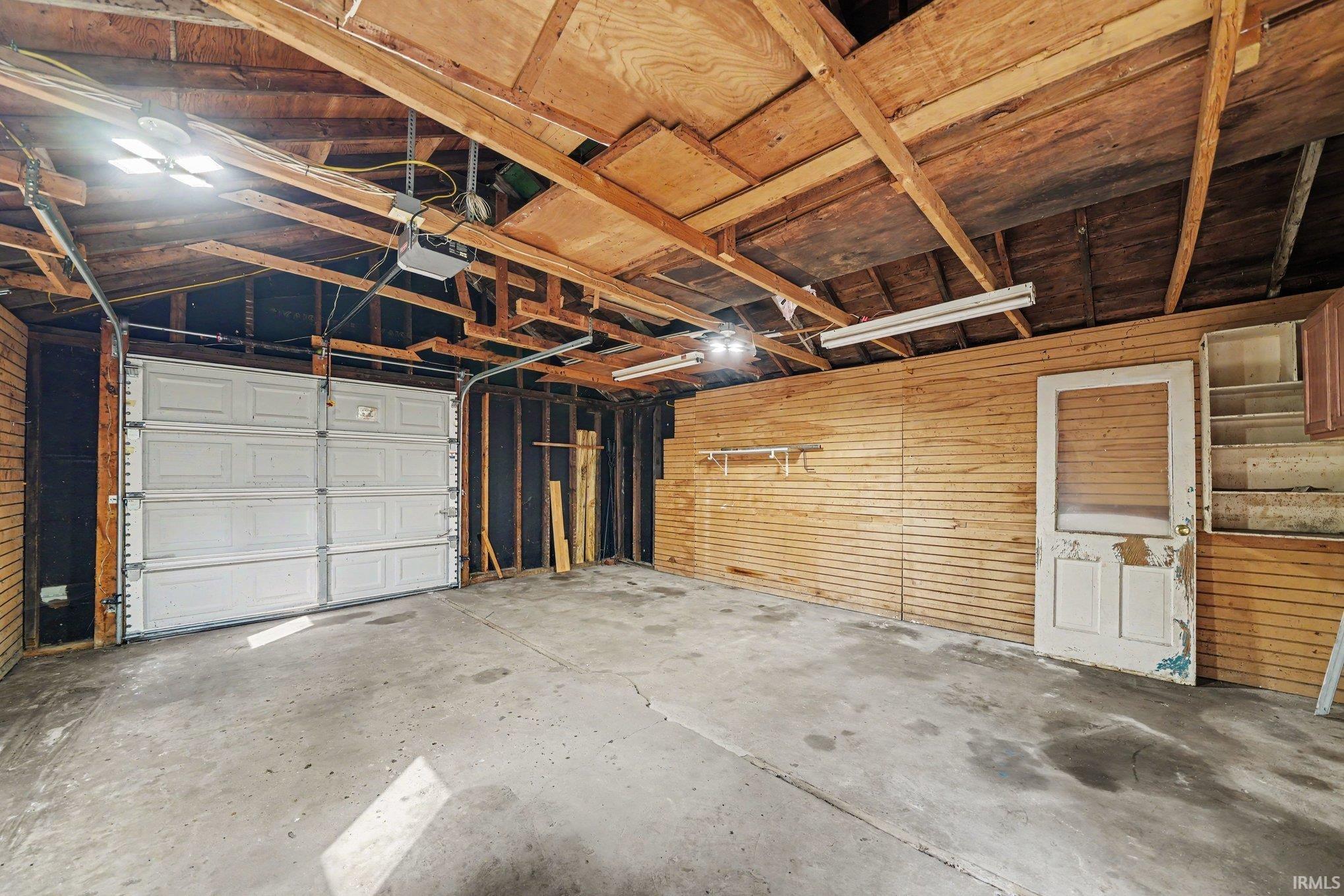 Garage with exposed wood rafter ceiling, concrete flooring, and a white paneled overhead door