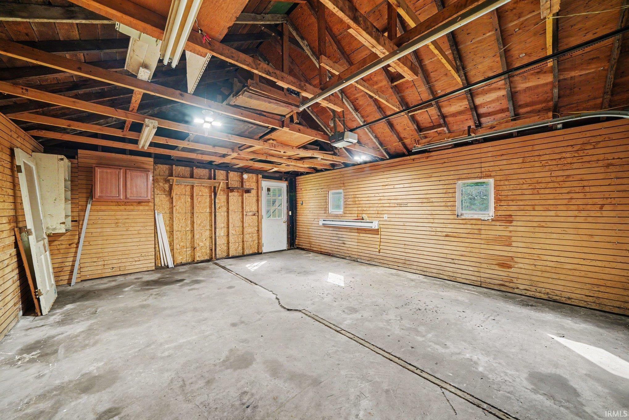 Spacious garage featuring exposed wood beam ceiling, concrete flooring, and built-in cabinetry