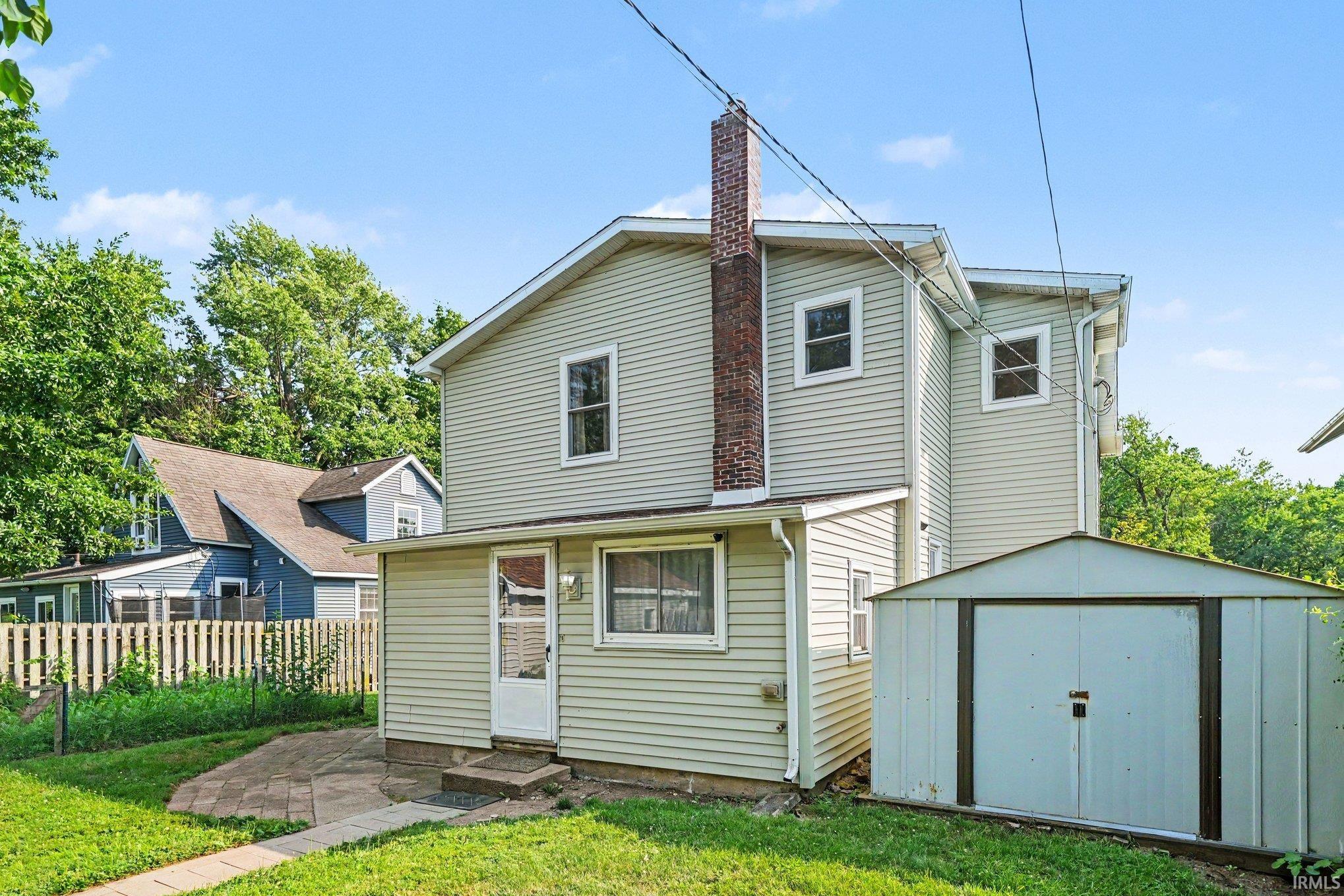 Rear exterior featuring light-colored siding, a brick chimney, and multiple windows