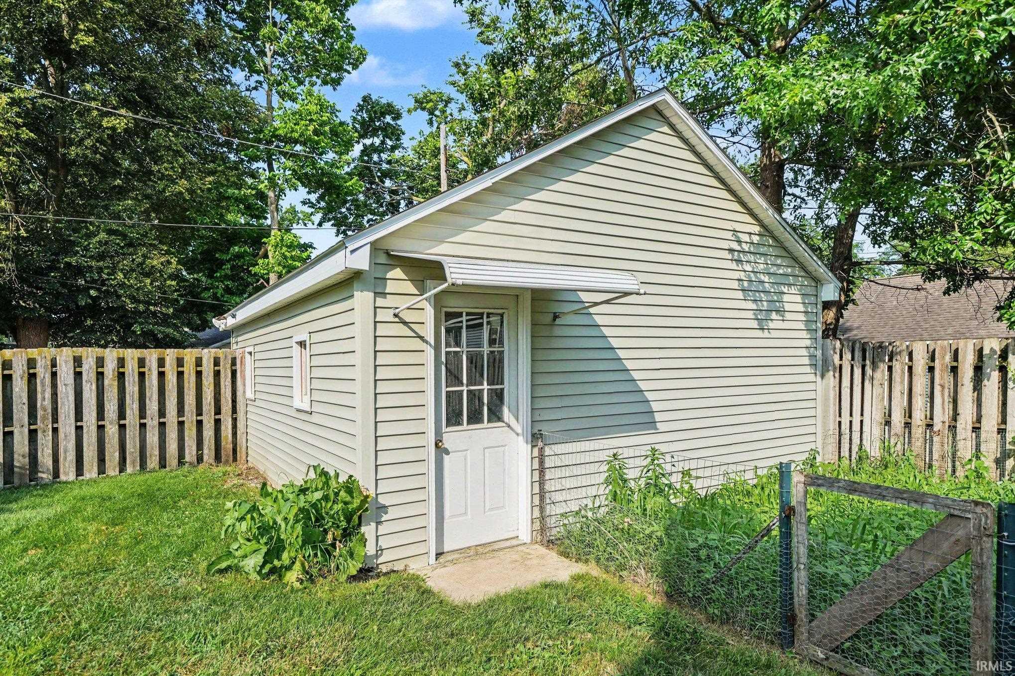 Detached outbuilding with vinyl siding, a gabled roof, and a single pane door with a metal awning