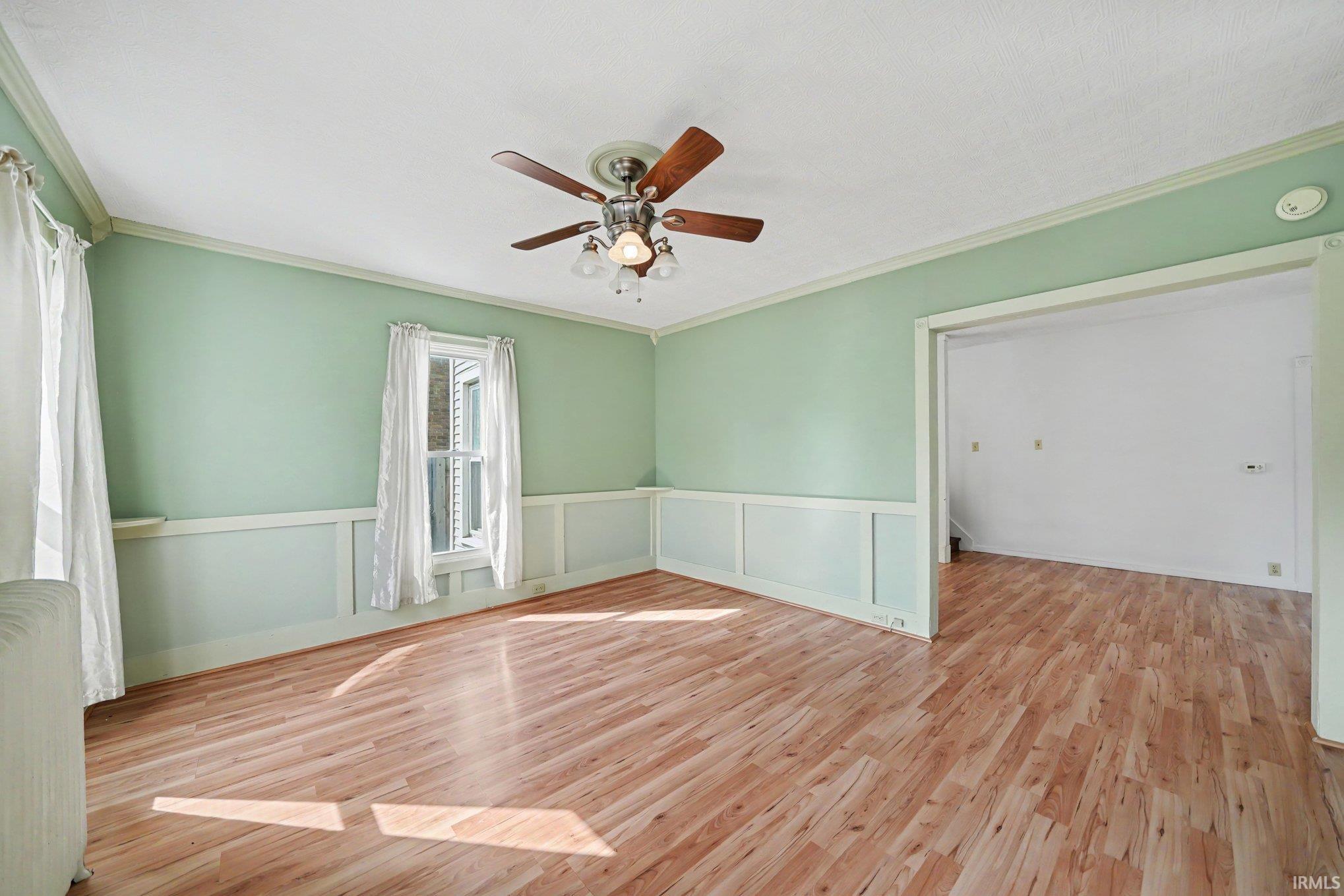 Spacious room featuring wood-finish flooring, light green walls with wainscoting, and a ceiling fan with light fixture