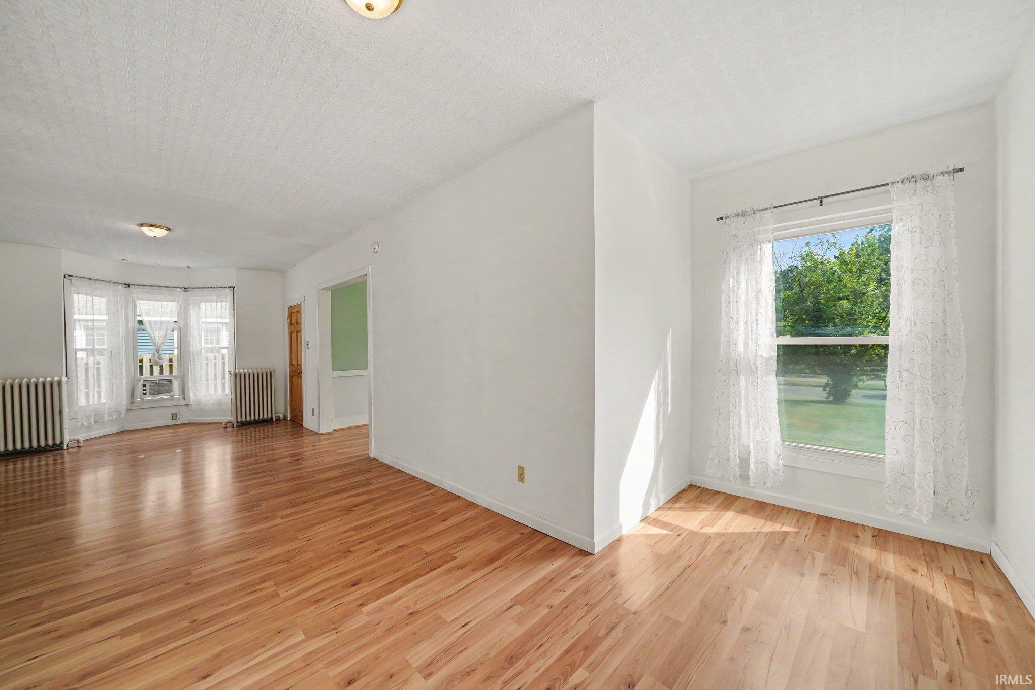 Spacious interior room featuring wood-finish flooring, white walls, and a bay window with multiple panes