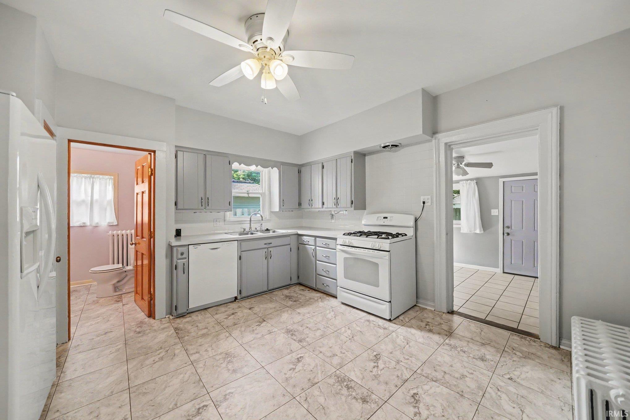 Kitchen featuring tile flooring, painted cabinetry, white appliances, and a ceiling fan with light fixture