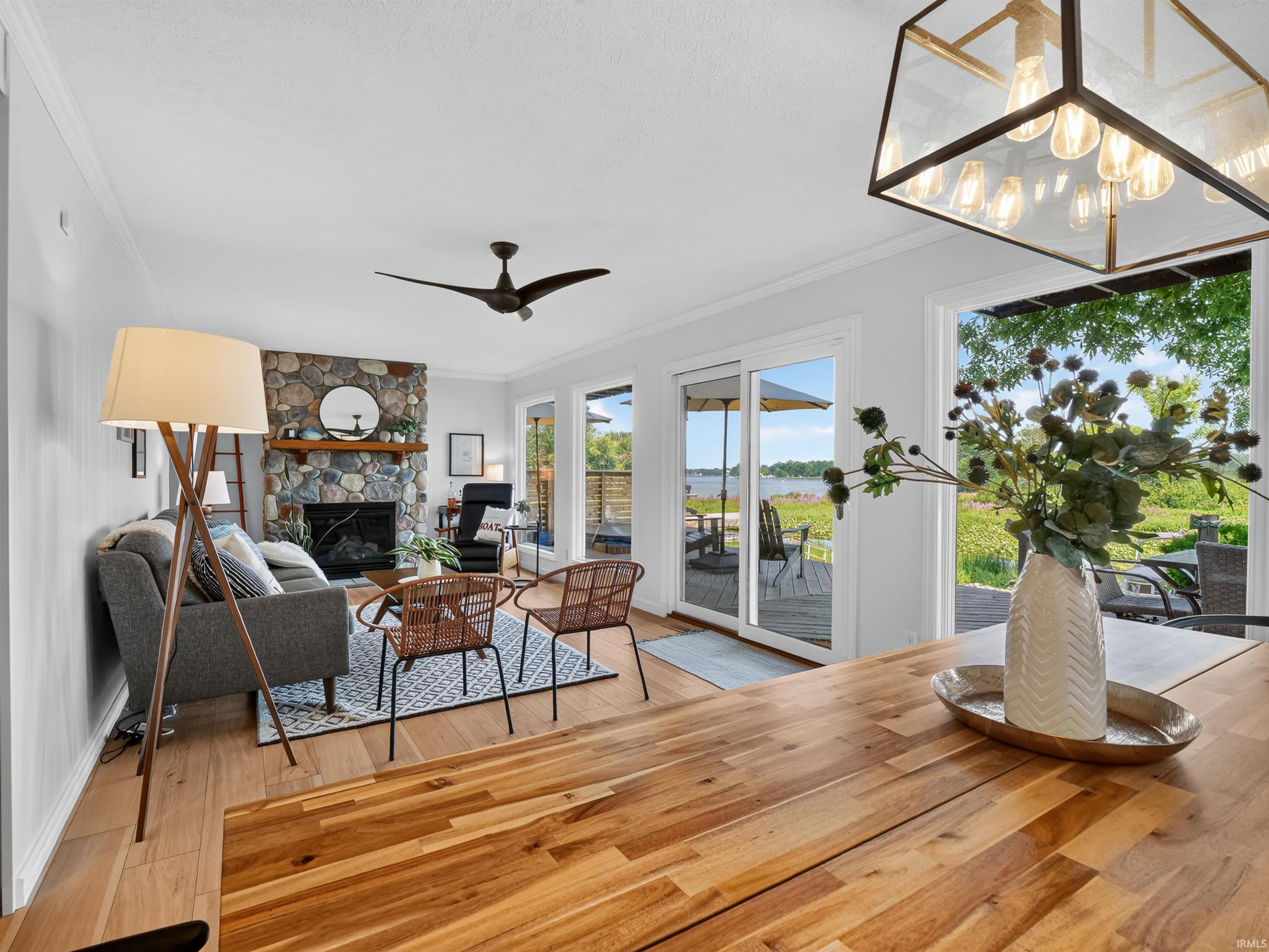 Open-concept living area featuring rich wood-finish flooring, a stone fireplace with wood mantel, and a multi-panel glass door providing access to an outdoor deck