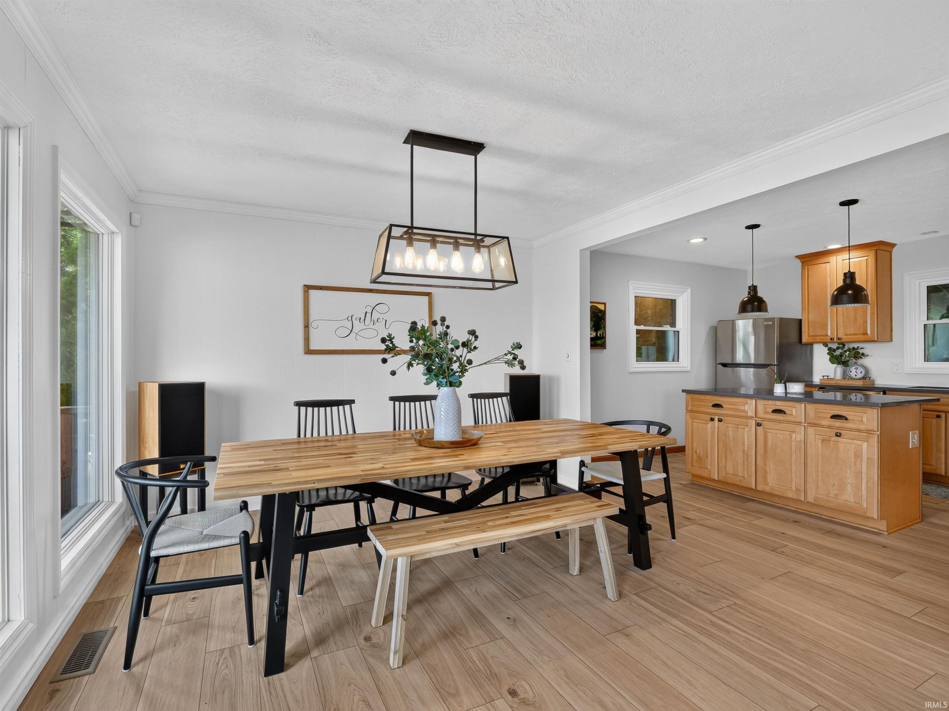 Open-concept dining area featuring wood-finish flooring, a modern linear chandelier, and ample natural light from large windows