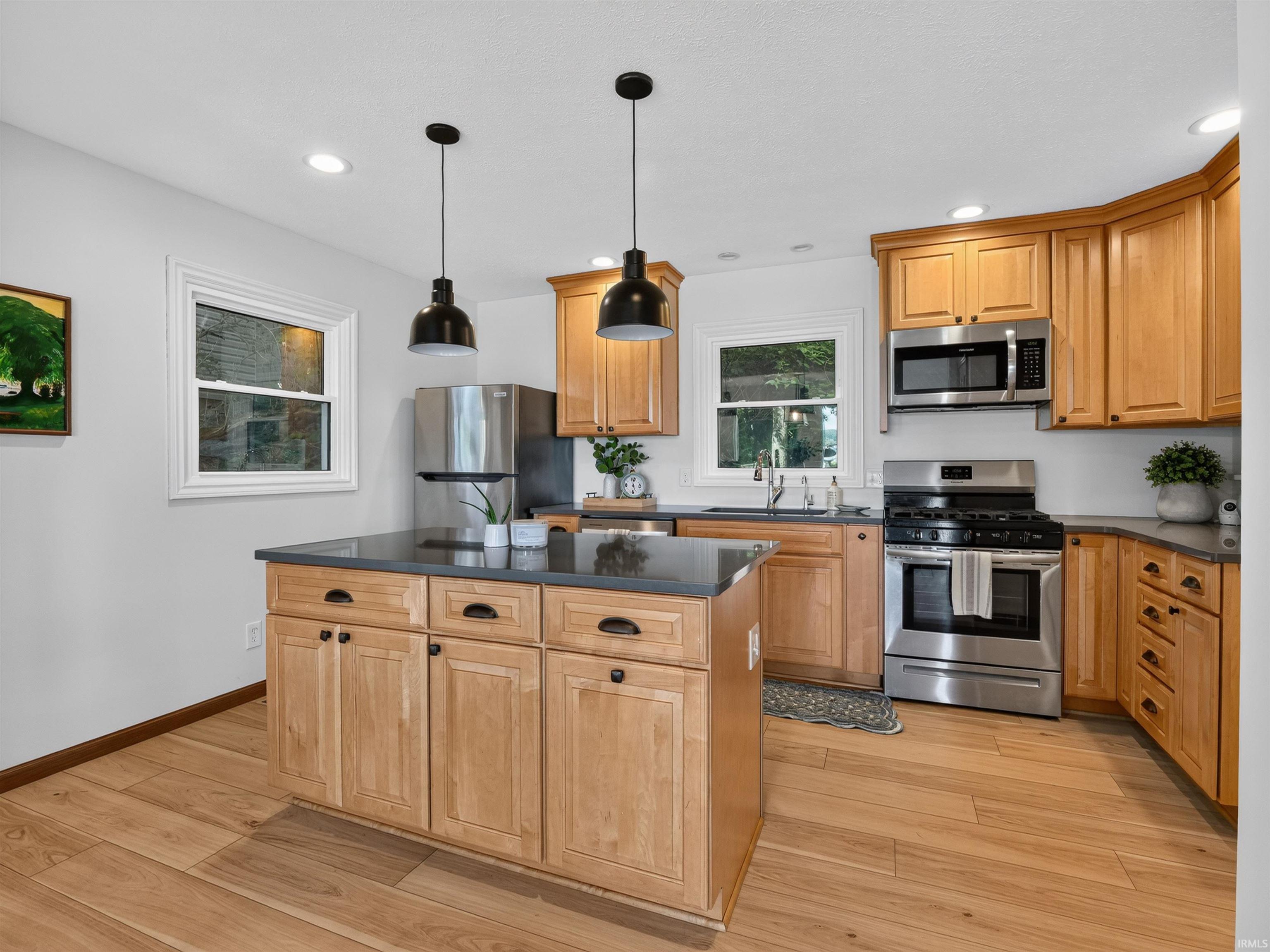 Kitchen featuring wood-finish flooring, light wood cabinetry, stainless steel appliances, a center island with dark countertops, and recessed lighting