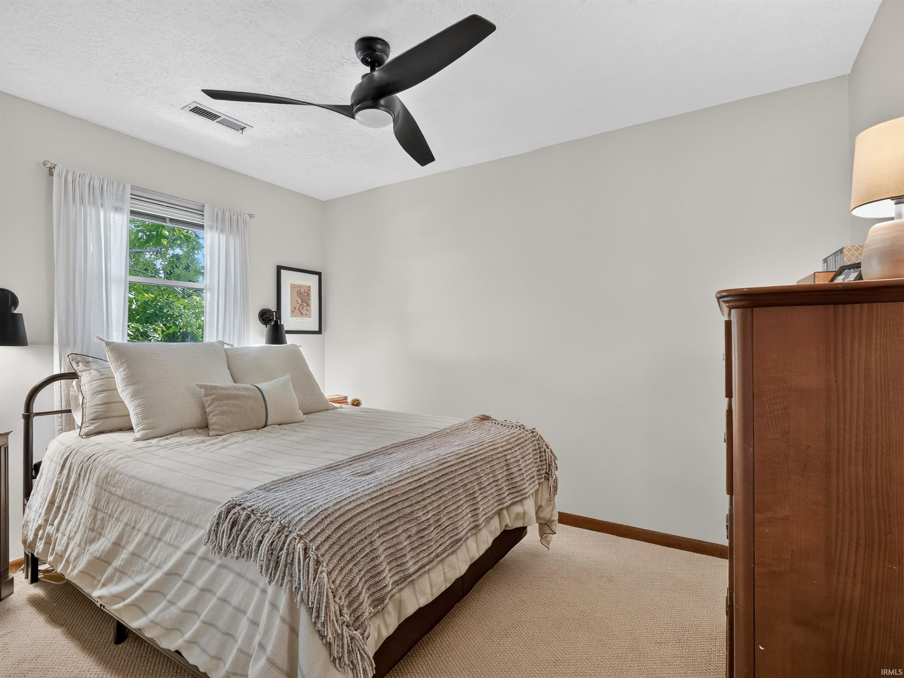 Carpeted room with a black ceiling fan, white walls, and a window with white sheer curtains