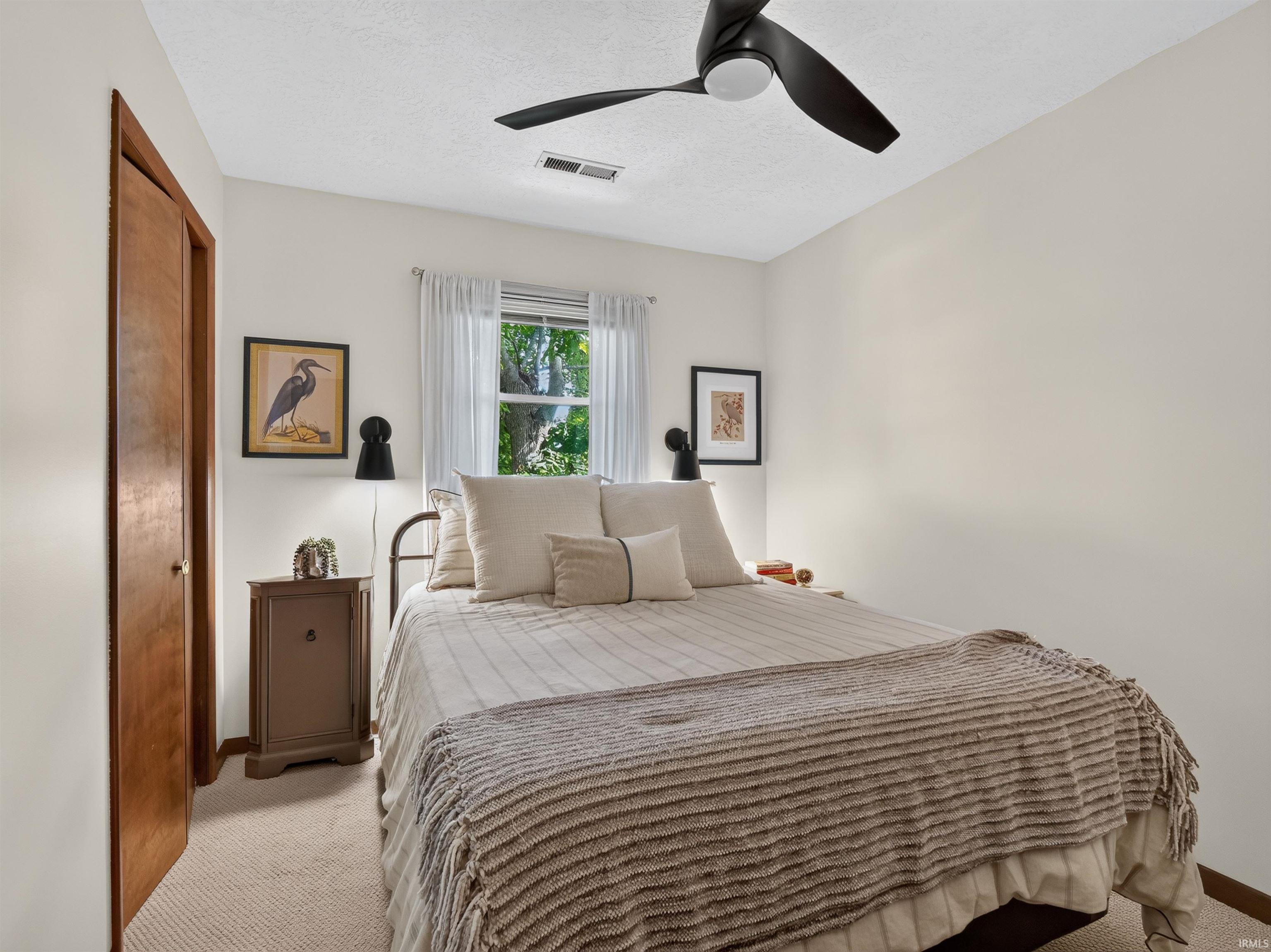 Bedroom featuring light-colored walls, ceiling fan, carpet flooring, window with sheer curtains, and a wood door