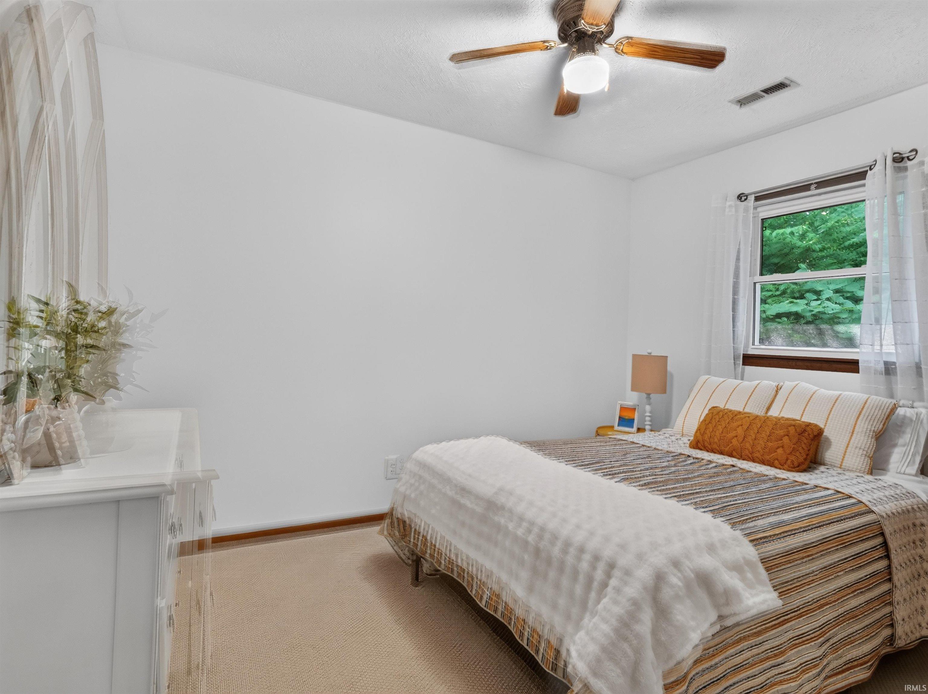 Carpeted bedroom featuring a ceiling fan with integrated lighting, a window with exterior tree scenery, and neutral wall finishes