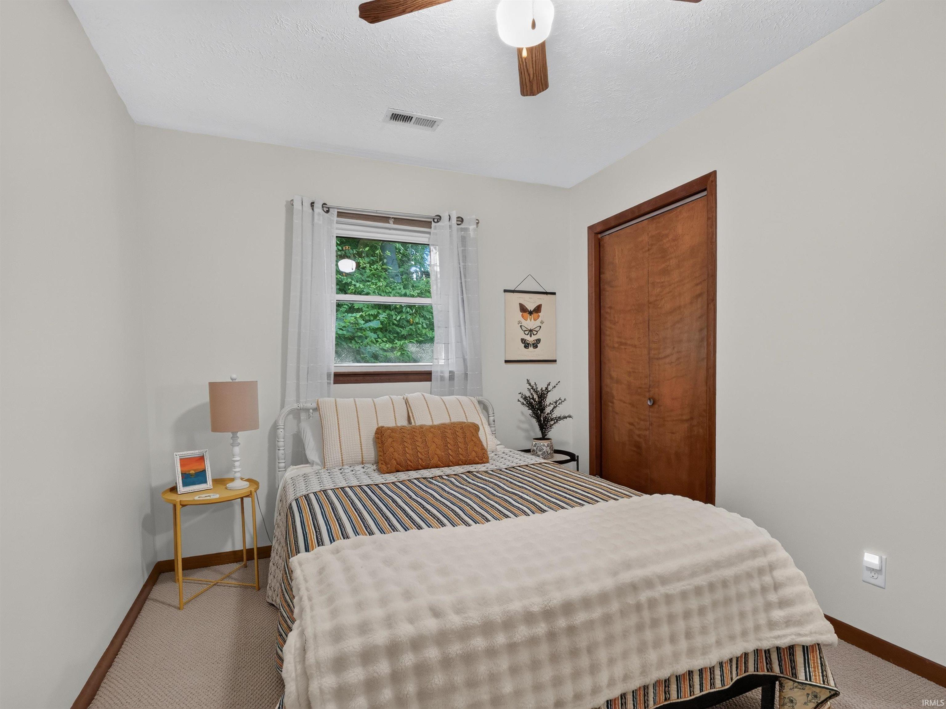 Bedroom featuring light neutral wall paint, wood-finish flooring, a window offering exterior views, and a ceiling fan with light fixture