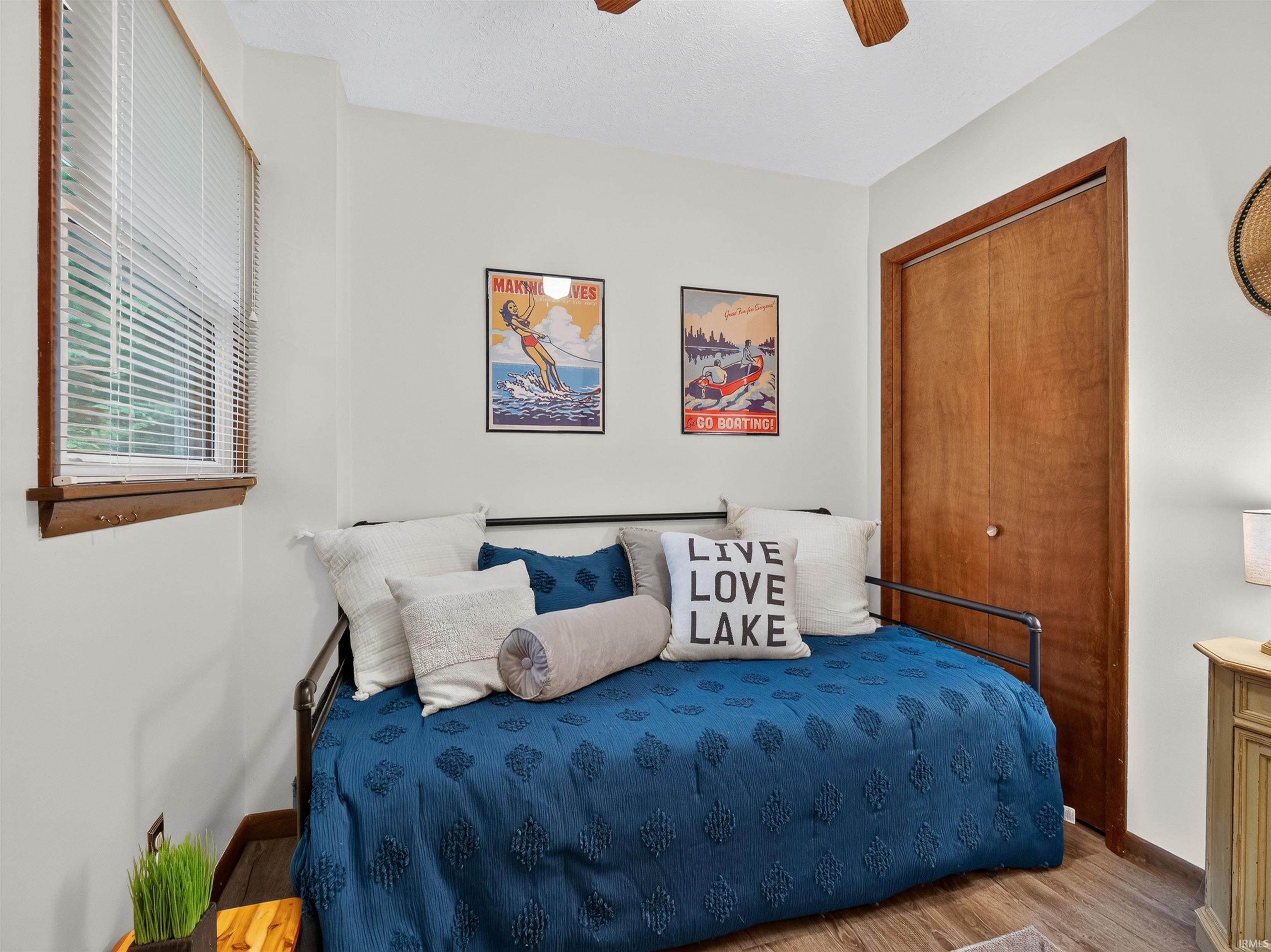 Interior room featuring wood-finish flooring, a window with horizontal blinds and wood trim, a wood-paneled bifold closet, and a ceiling fan