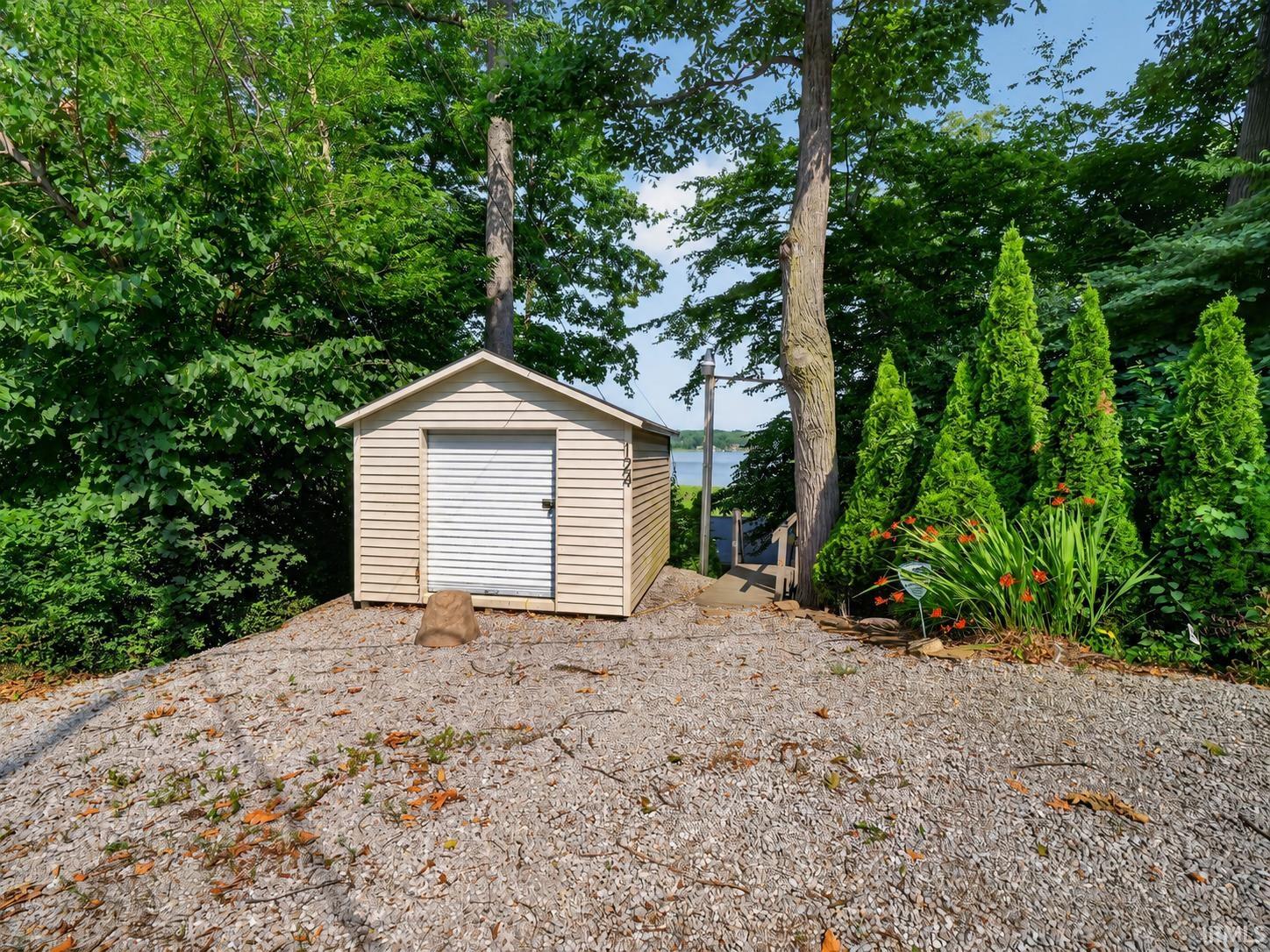Gravel driveway leading to a detached storage shed with a roll-up door