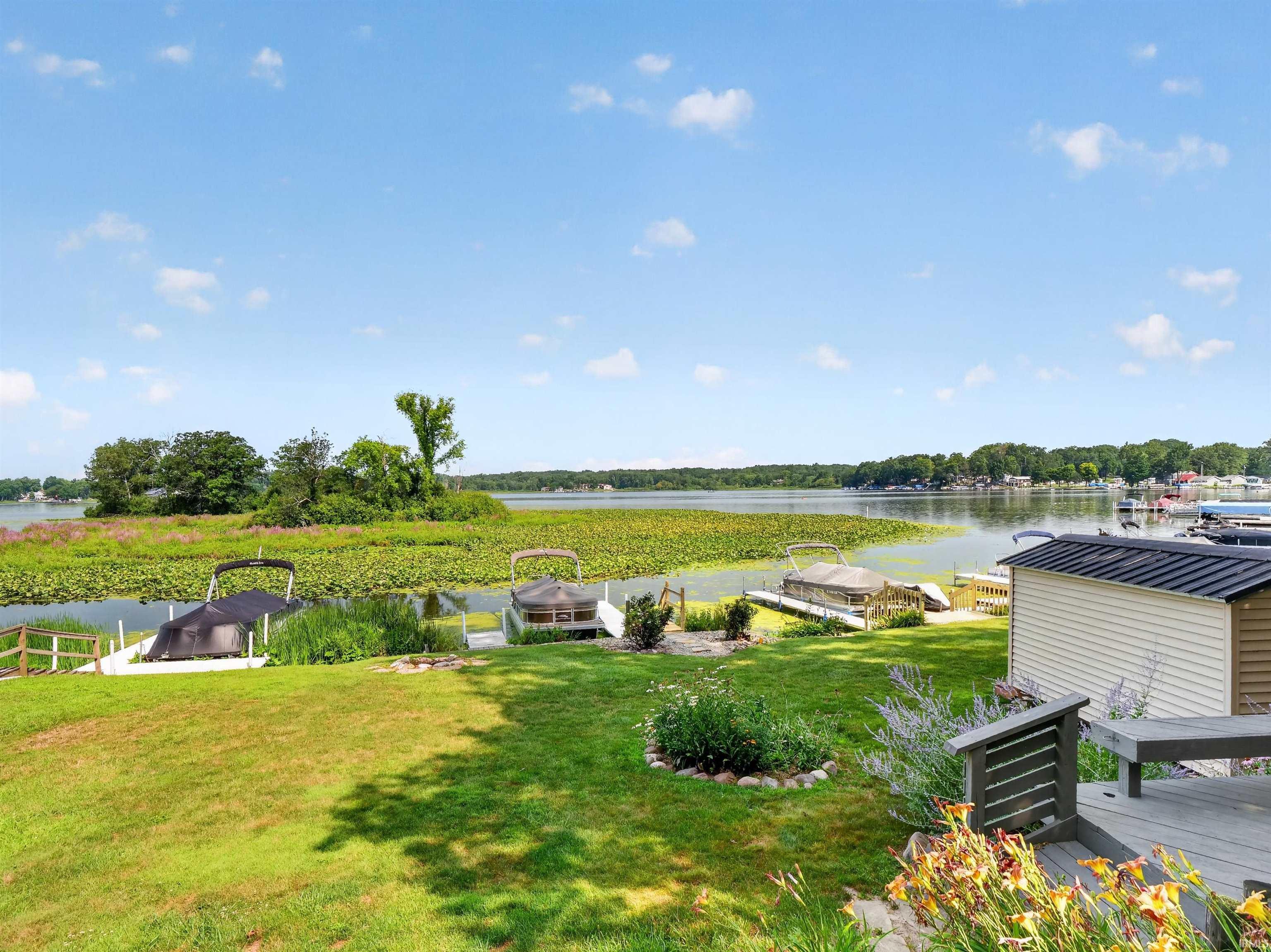 Expansive waterfront lawn featuring boat docks, mature landscaping, and a waterside shed