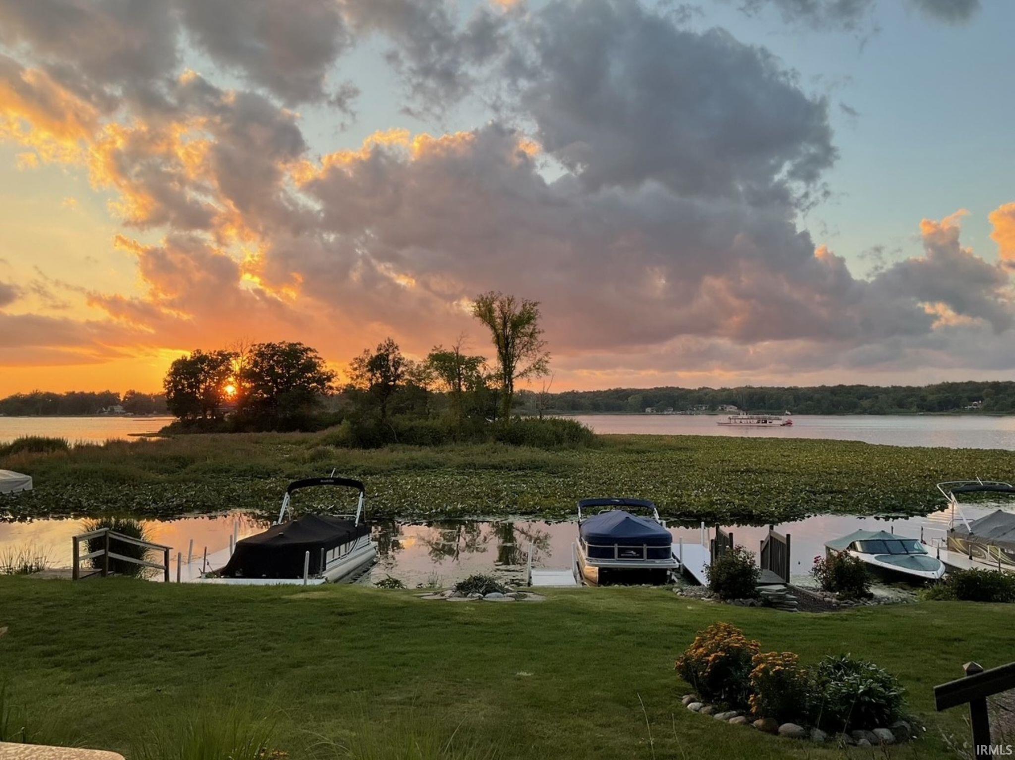 Waterfront property featuring a landscaped lawn leading to a lake with multiple boat slips and mature trees on the opposing shore
