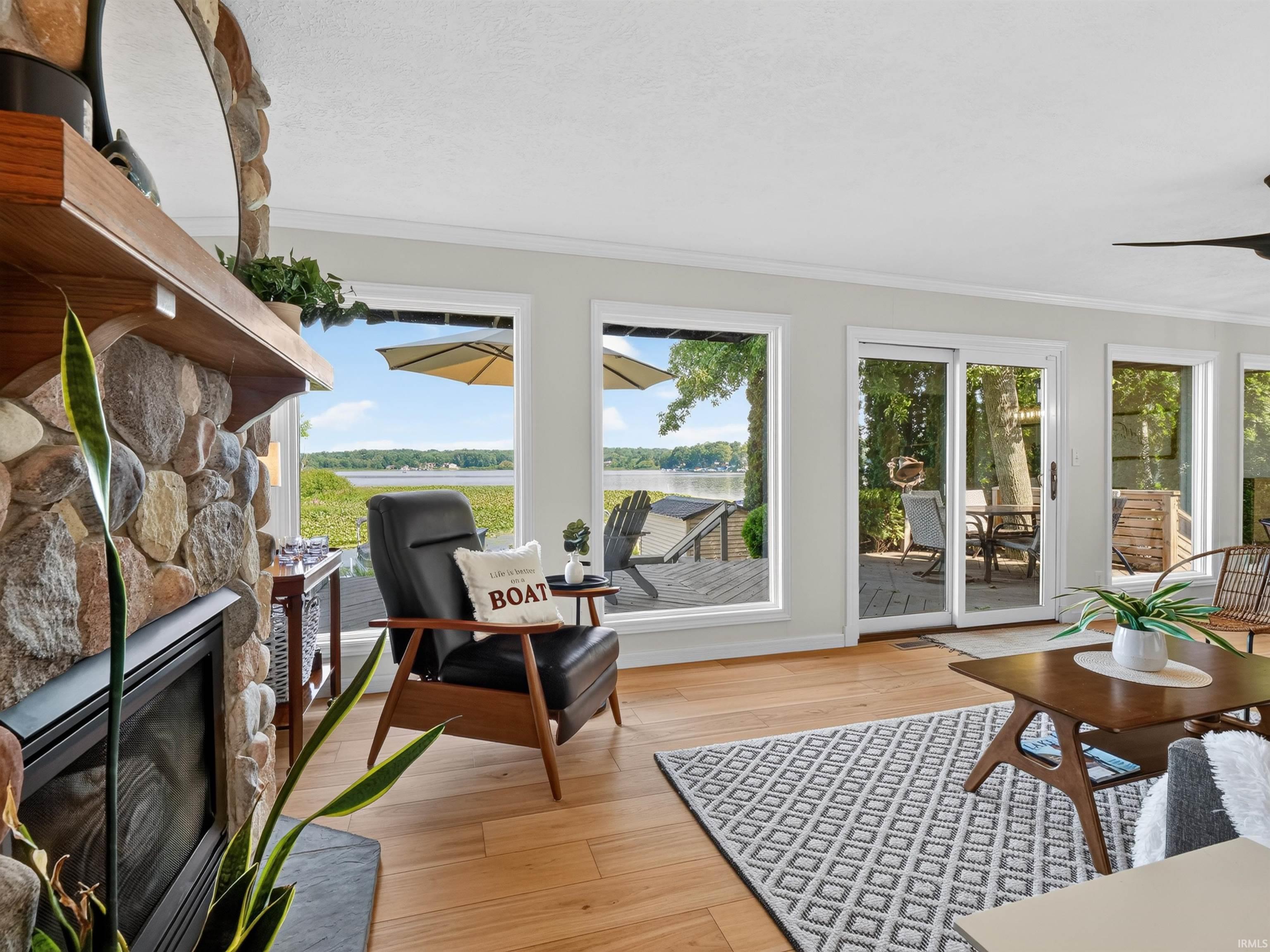 Expansive living space featuring light wood-finish flooring, a stone fireplace, and ample natural light from multiple windows and sliding glass doors