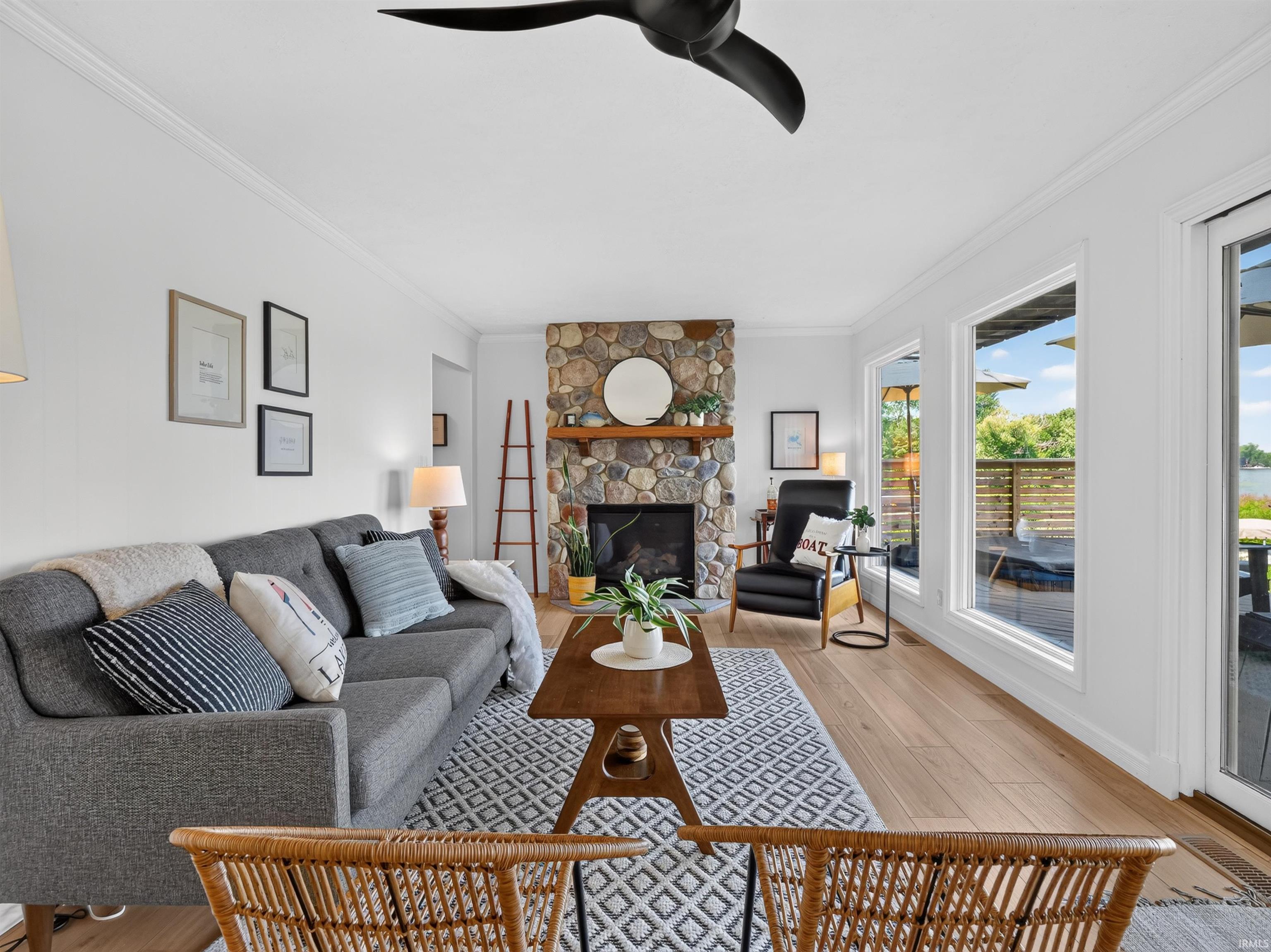 Living room featuring a stone-clad fireplace with a wood mantle, wood-finish flooring, and crown molding