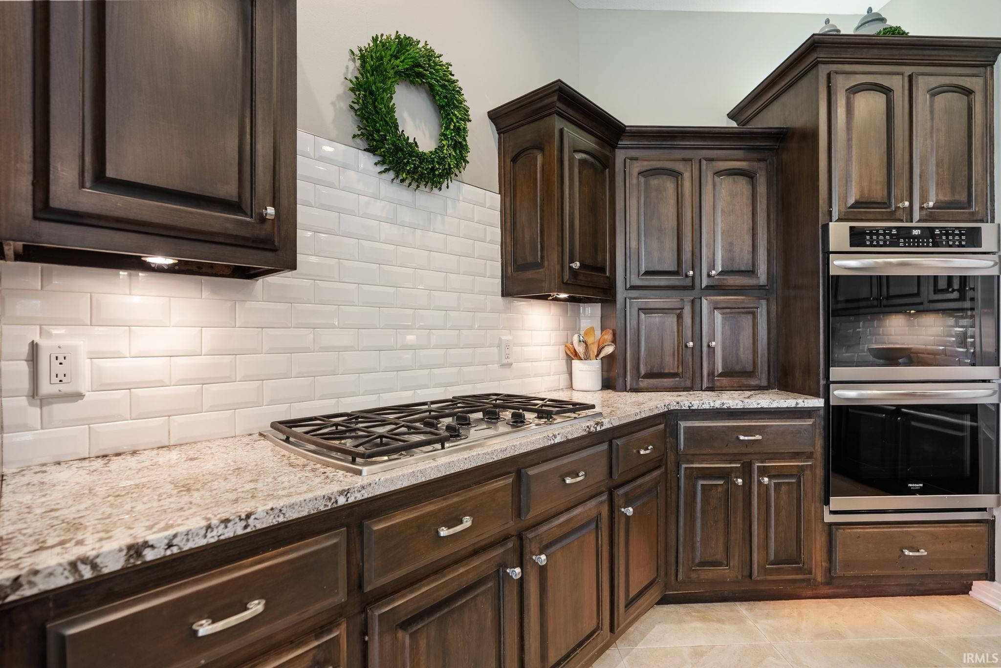 Kitchen featuring dark wood cabinetry, light granite countertops, a gas cooktop, and a double wall oven