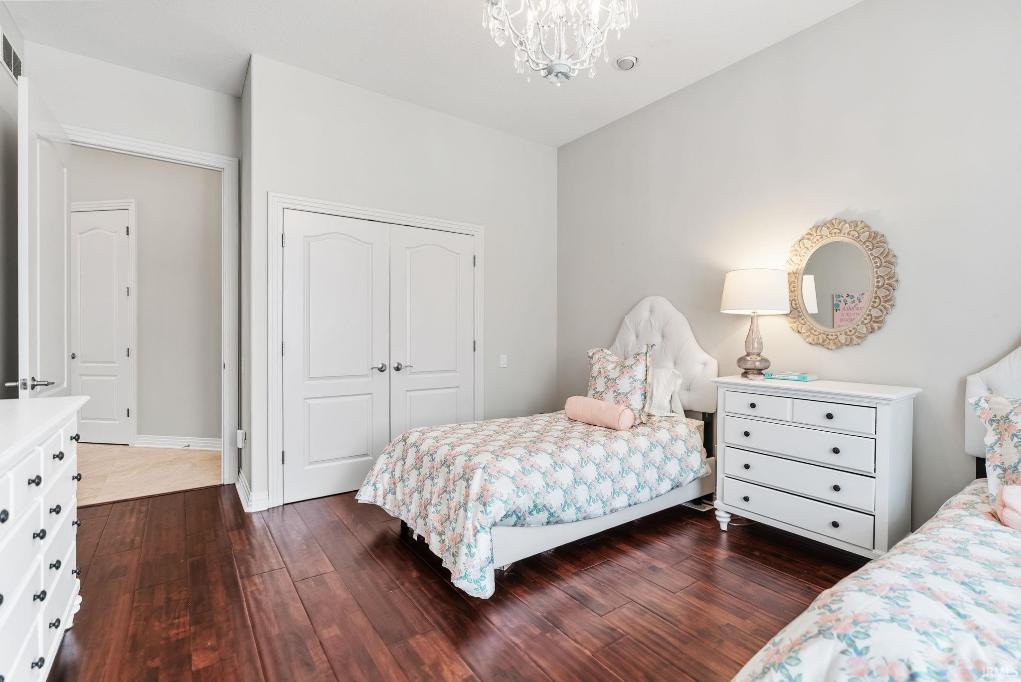 Bedroom featuring rich wood-finish flooring, light grey wall paint, and a crystal chandelier