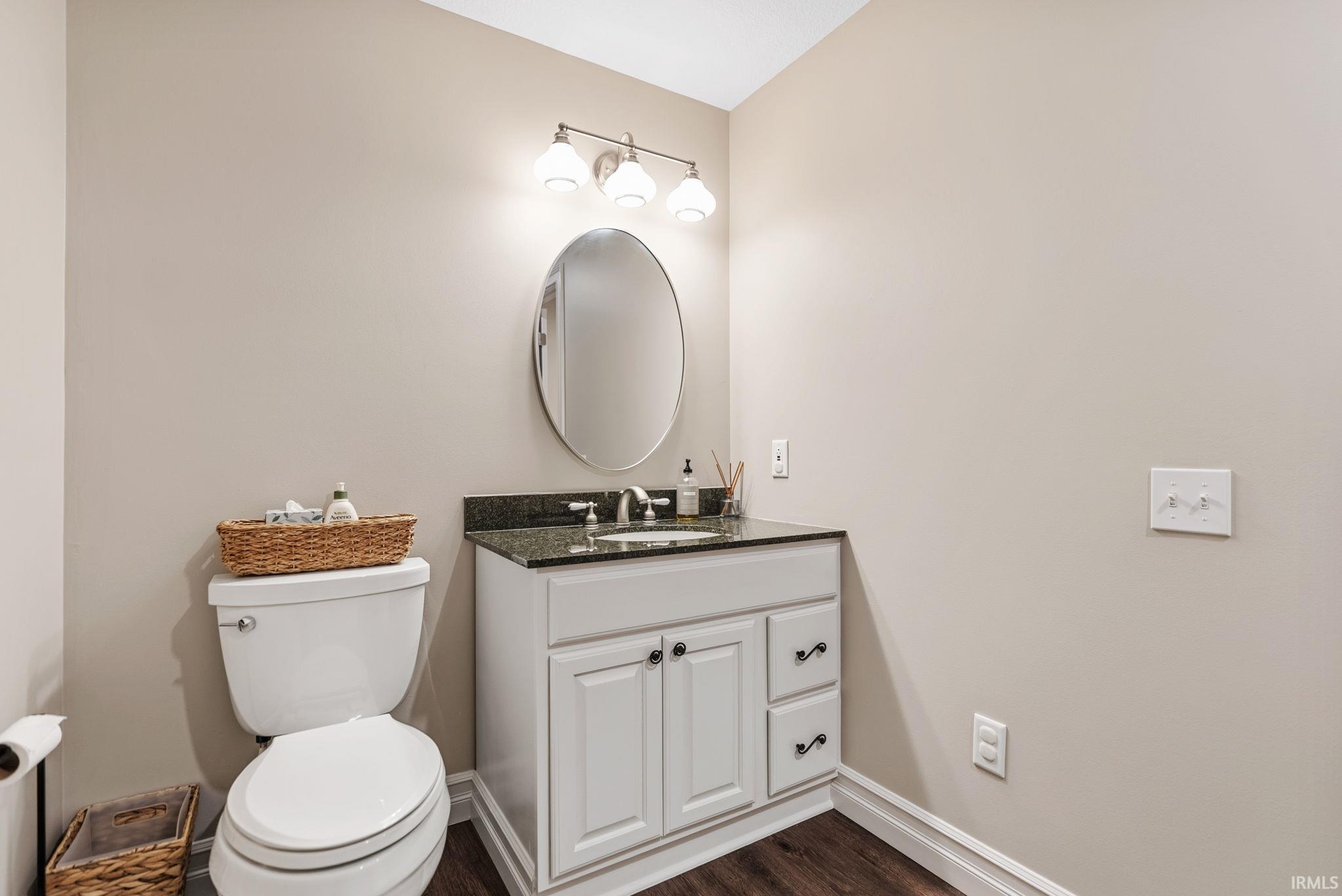 Bathroom featuring a white toilet, white vanity with dark countertop, an oval mirror, and a three-light vanity fixture