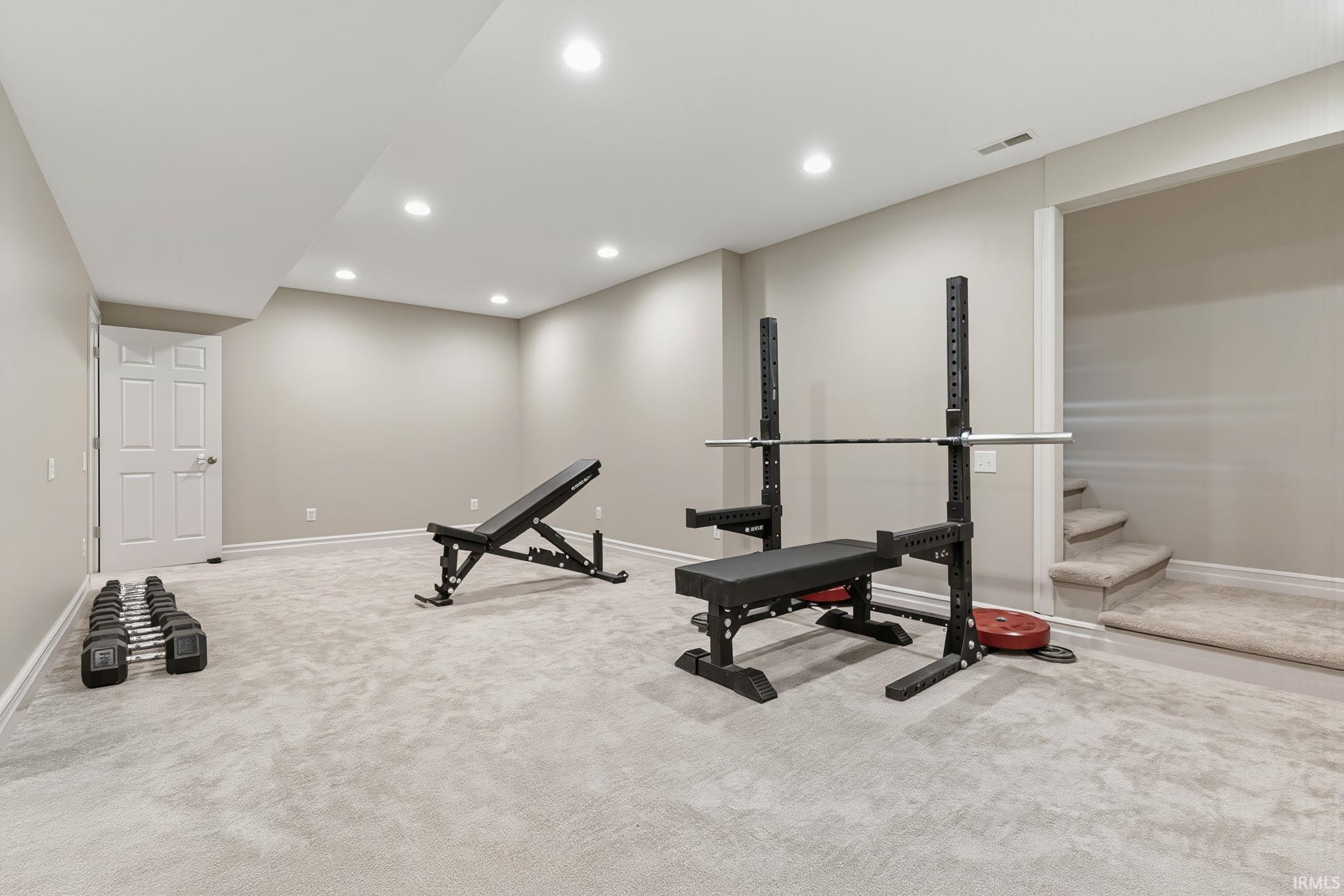 Spacious carpeted room with recessed lighting, light neutral wall tones, white trim, and a paneled door