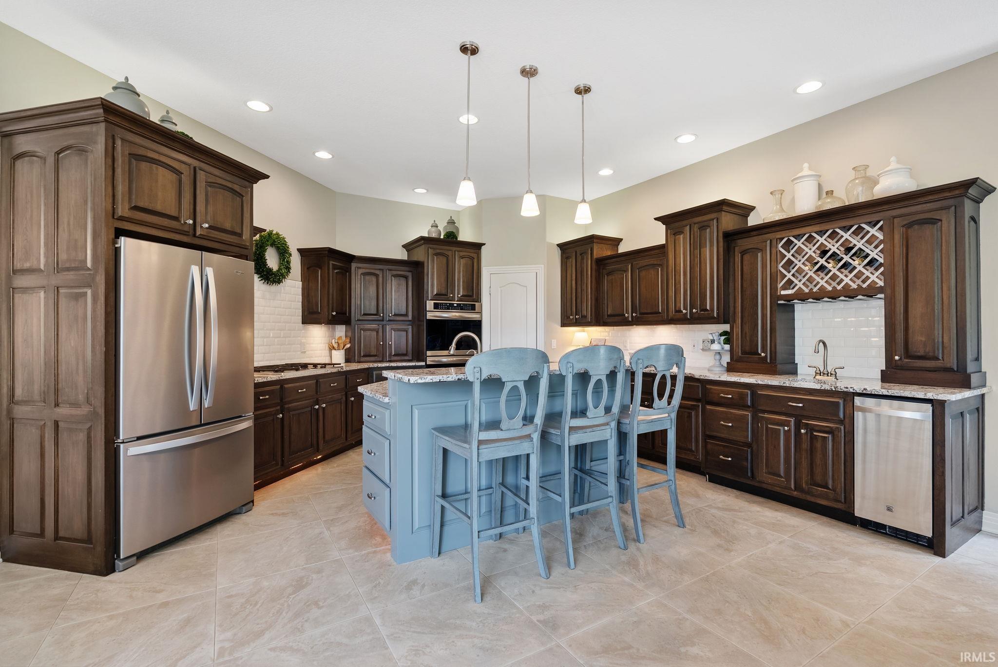 Kitchen featuring a blue island with seating, dark wood cabinetry, stainless steel appliances, white subway tile backsplash, and light tile flooring