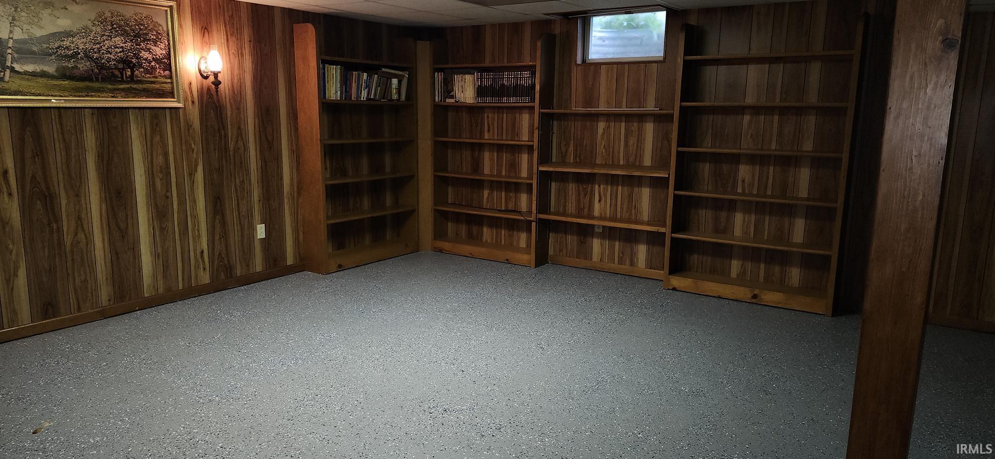 Room featuring extensive built-in wooden shelving, wood-paneled walls, and speckled flooring