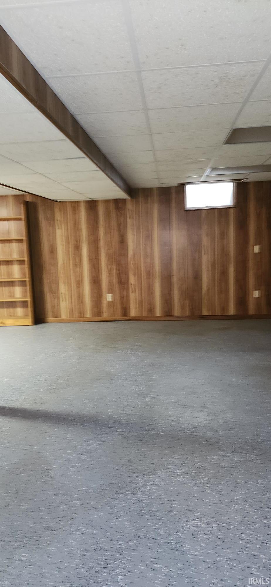 Spacious room featuring wood-panel walls, acoustic tile ceiling, and resilient flooring
