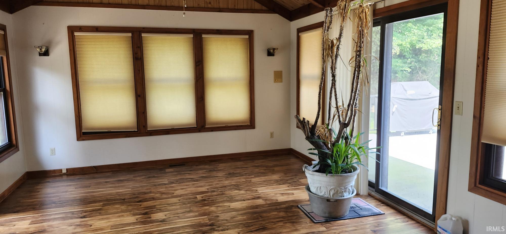 Sunlit room featuring wood-finish flooring, a vaulted wood-paneled ceiling, multiple large windows with natural wood frames, and a glass sliding door providing outdoor access