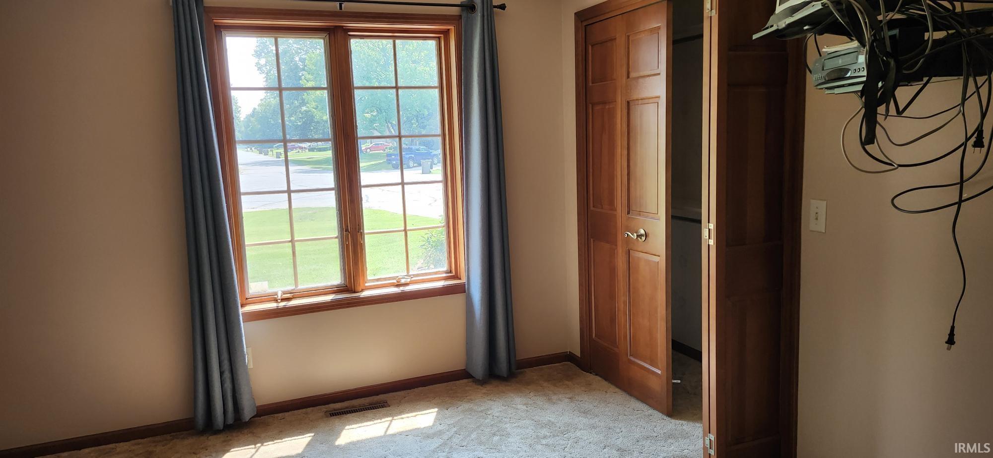 Carpeted room featuring a multi-pane window with wood-finish trim, a wood-finish bi-fold closet door, and light-toned walls