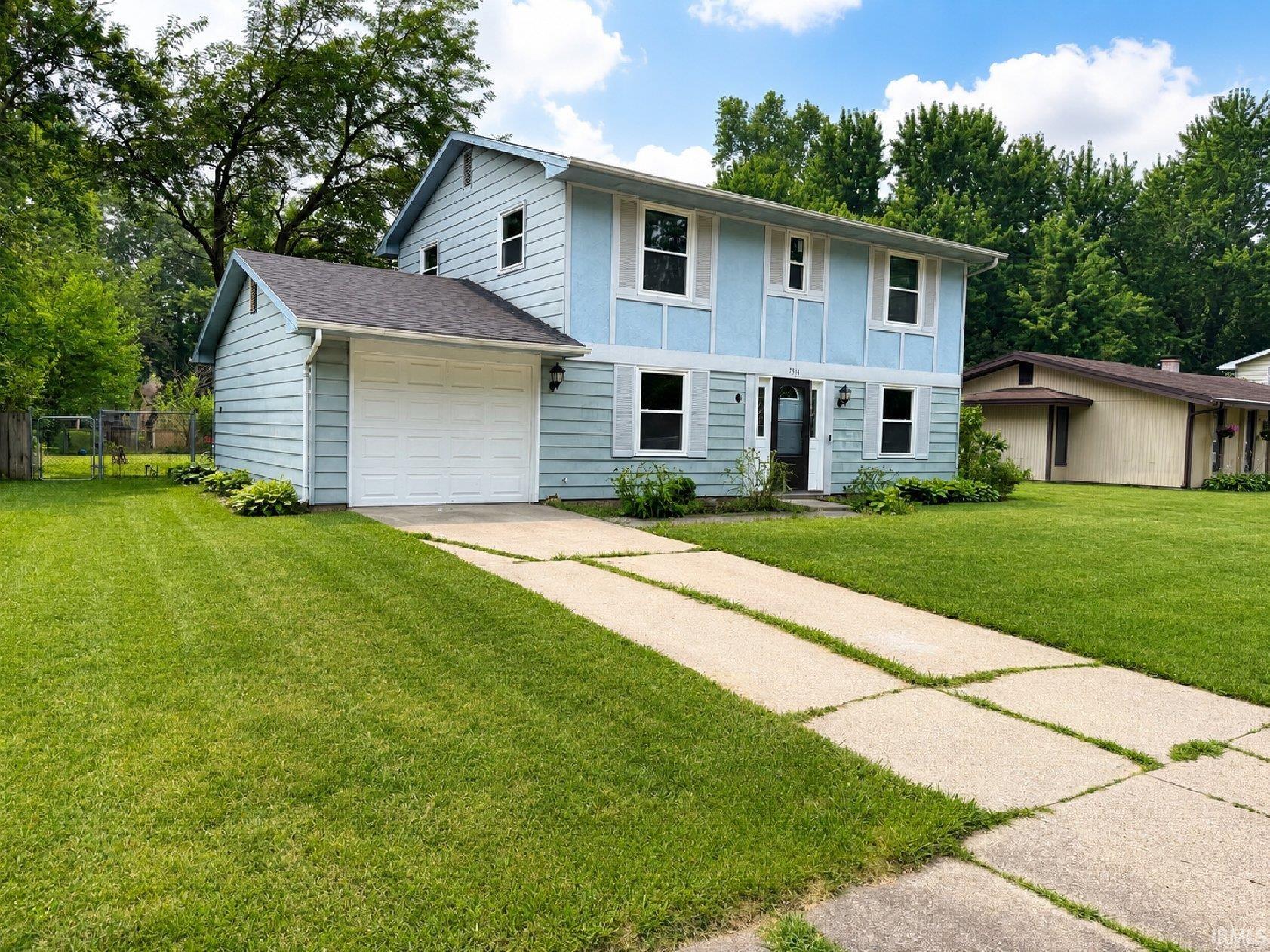 Two-story split-level home featuring light blue siding with white trim accents and a dark roof