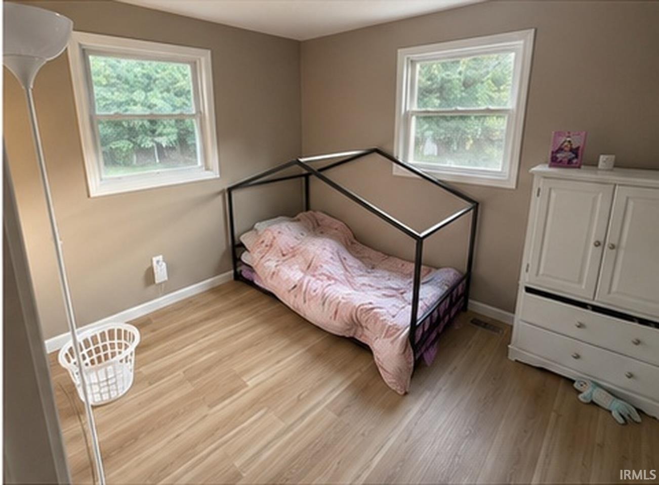 Light wood-finish flooring complements the neutral wall color in this room, featuring two windows with white trim