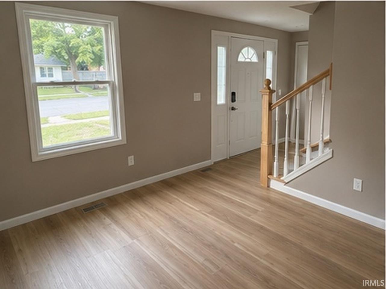 Entryway featuring wood-finish flooring, a white front door with sidelights and transom, a double-hung window, and a staircase with a wood handrail and white balusters