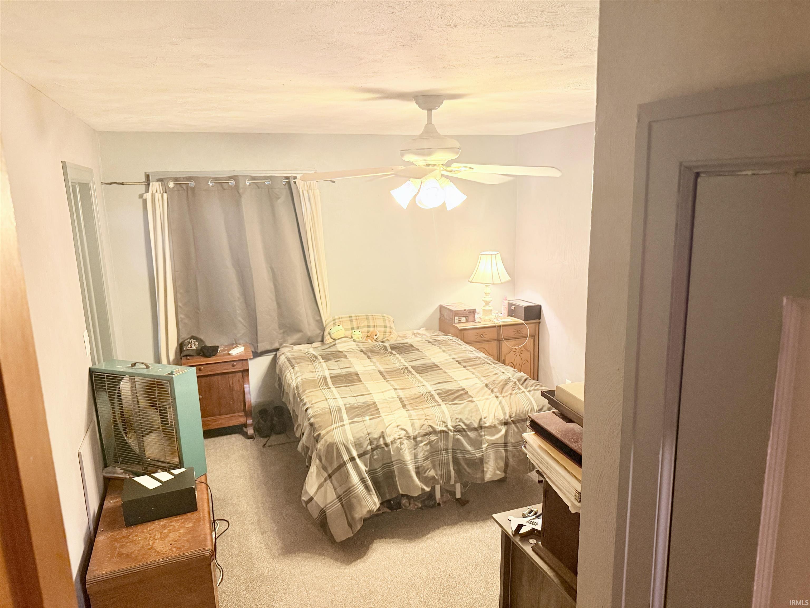 Carpeted bedroom featuring a ceiling fan with integrated lighting, a window with drapery, and painted walls