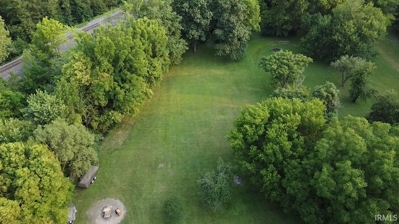 Expansive green space featuring a large grassy lawn, mature deciduous trees, and a gravel fire pit area