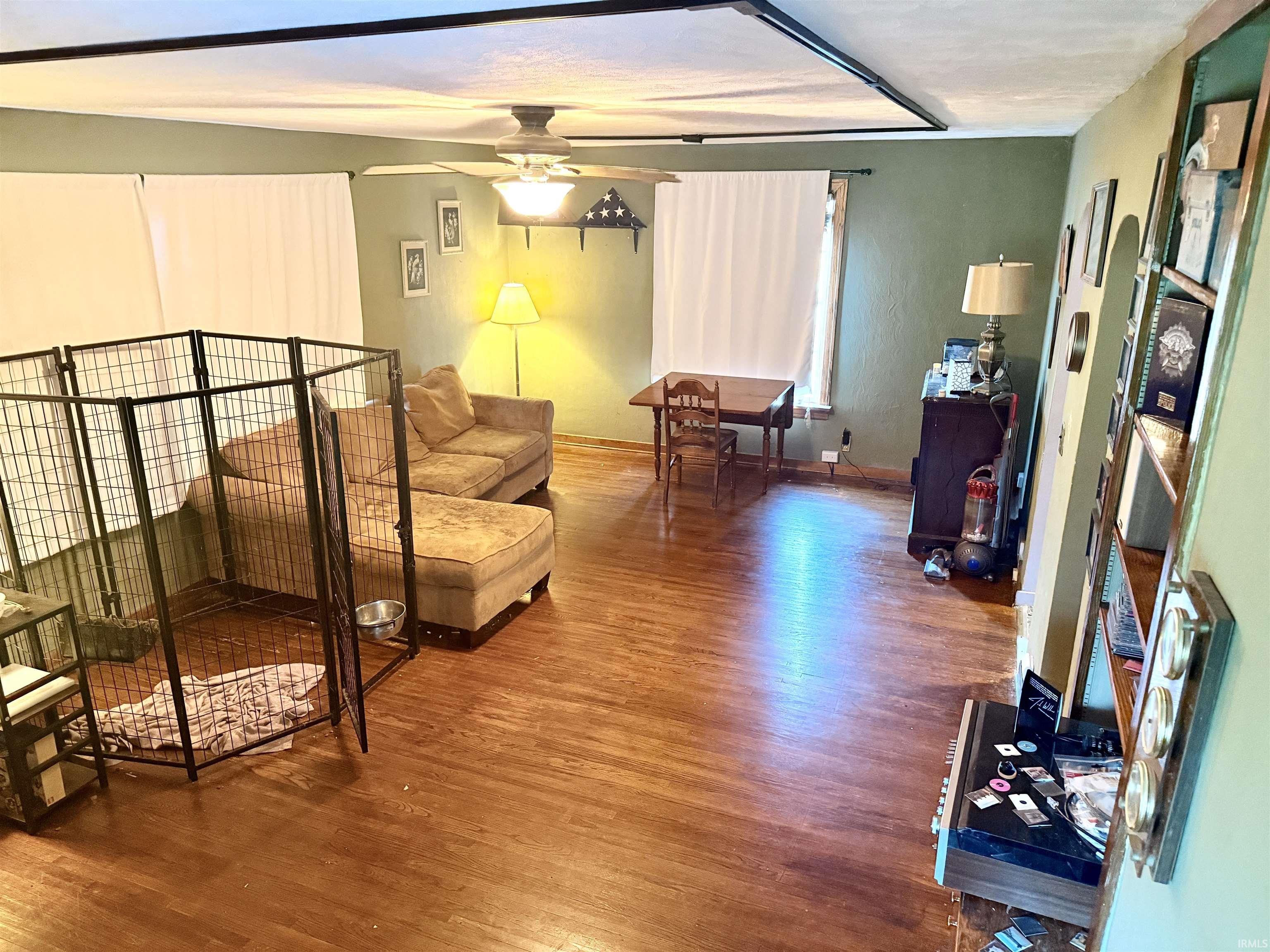 Spacious room featuring wood-finish flooring, a ceiling fan with integrated lighting, and multiple windows with privacy coverings