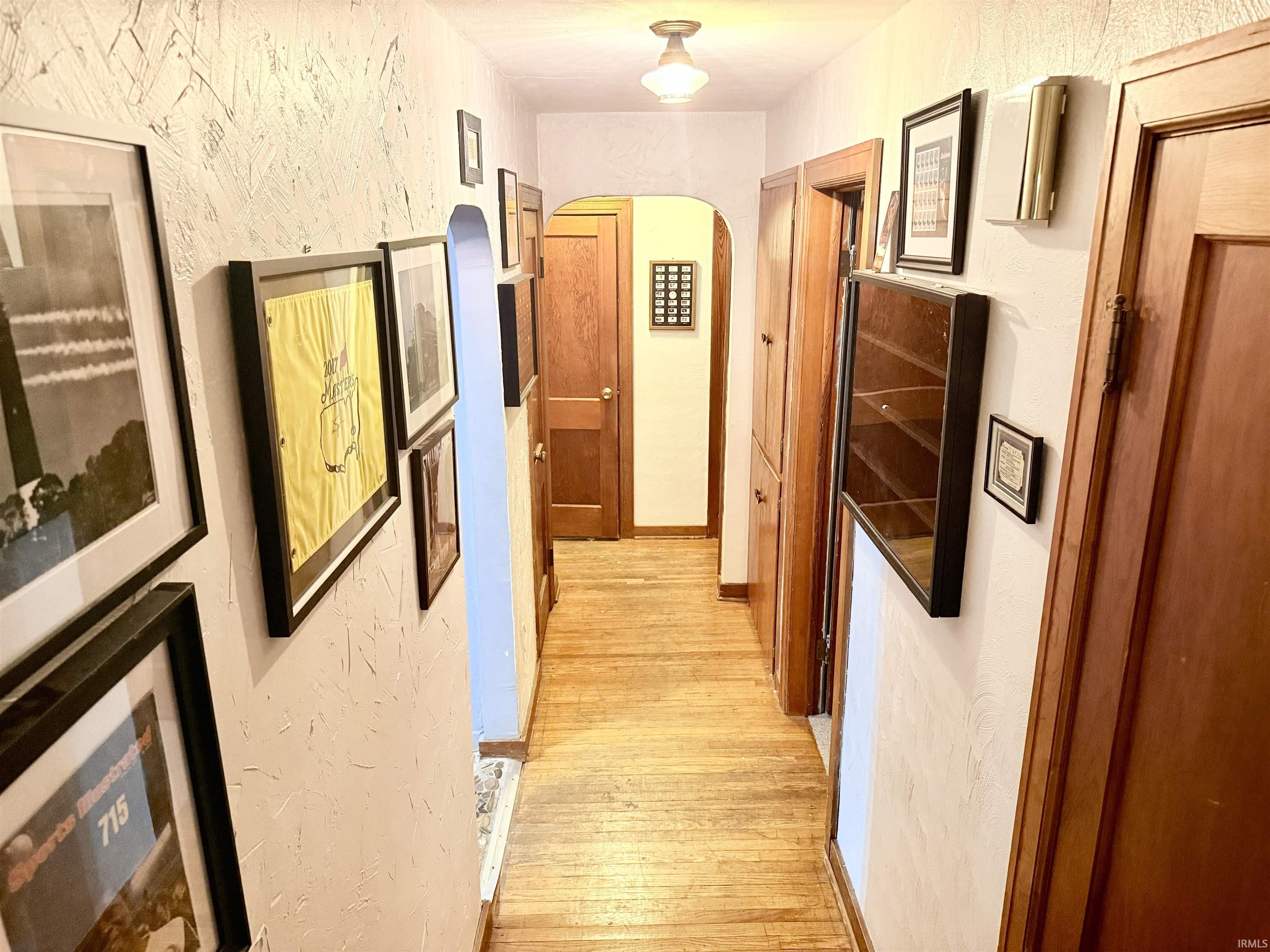 Hardwood flooring extending through a hallway with wood-paneled doors and an arched doorway