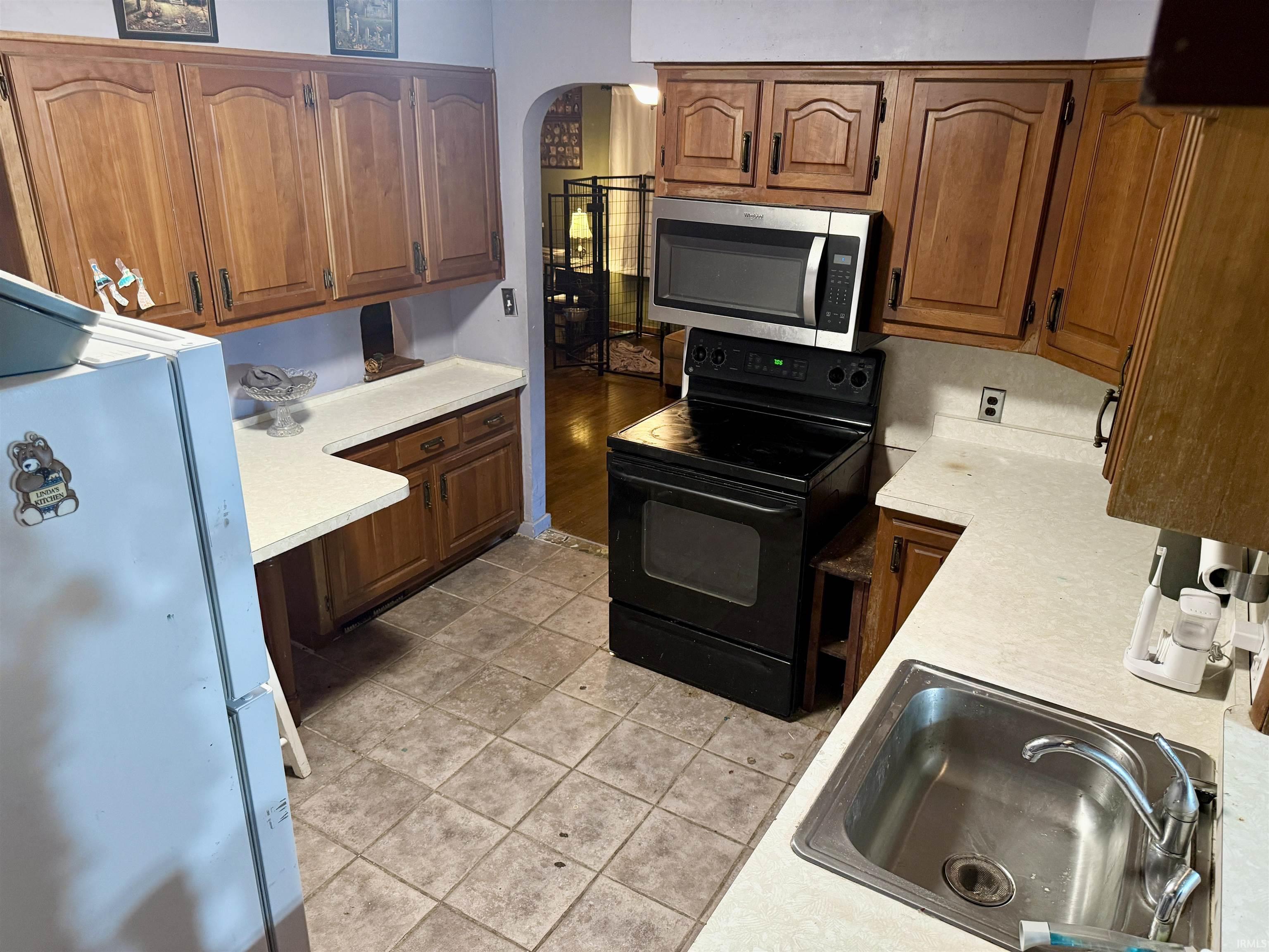 Kitchen featuring wood-finish cabinetry, light-toned countertops, a stainless steel sink with a modern faucet, and a black electric range with an overhead microwave