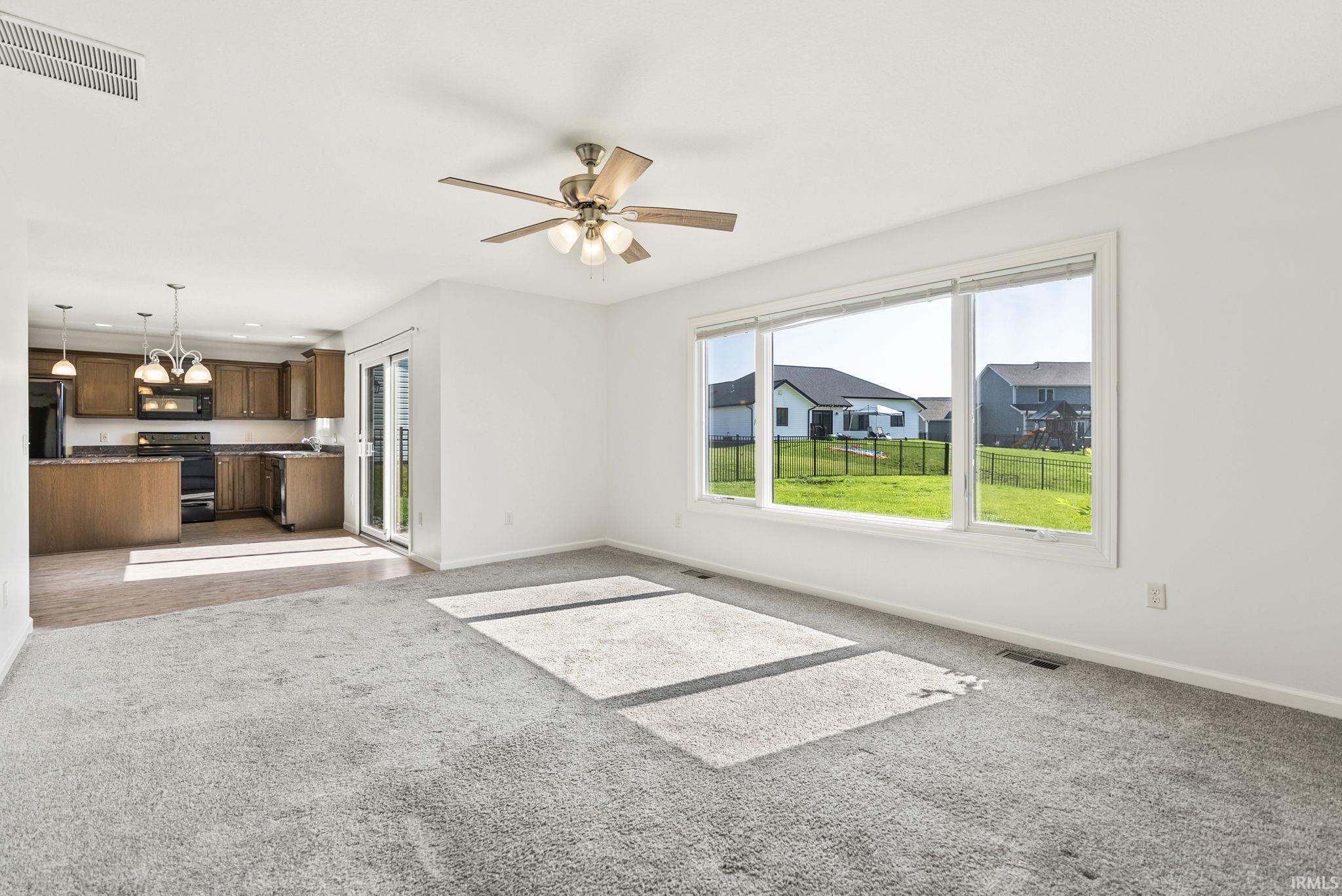 Open-concept living area featuring a large window, a ceiling fan, and grey carpeting
