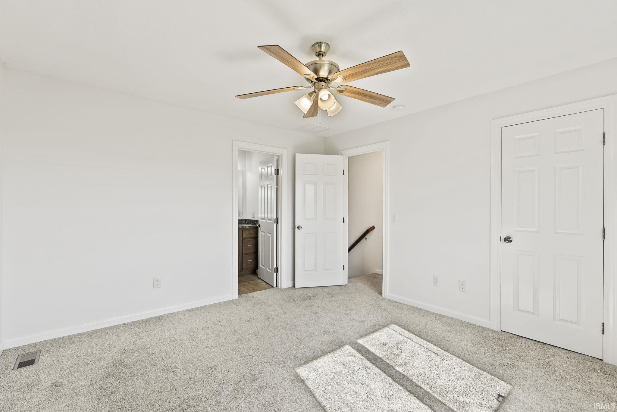 Carpeted room featuring a ceiling fan with light fixture, white walls, and white trim