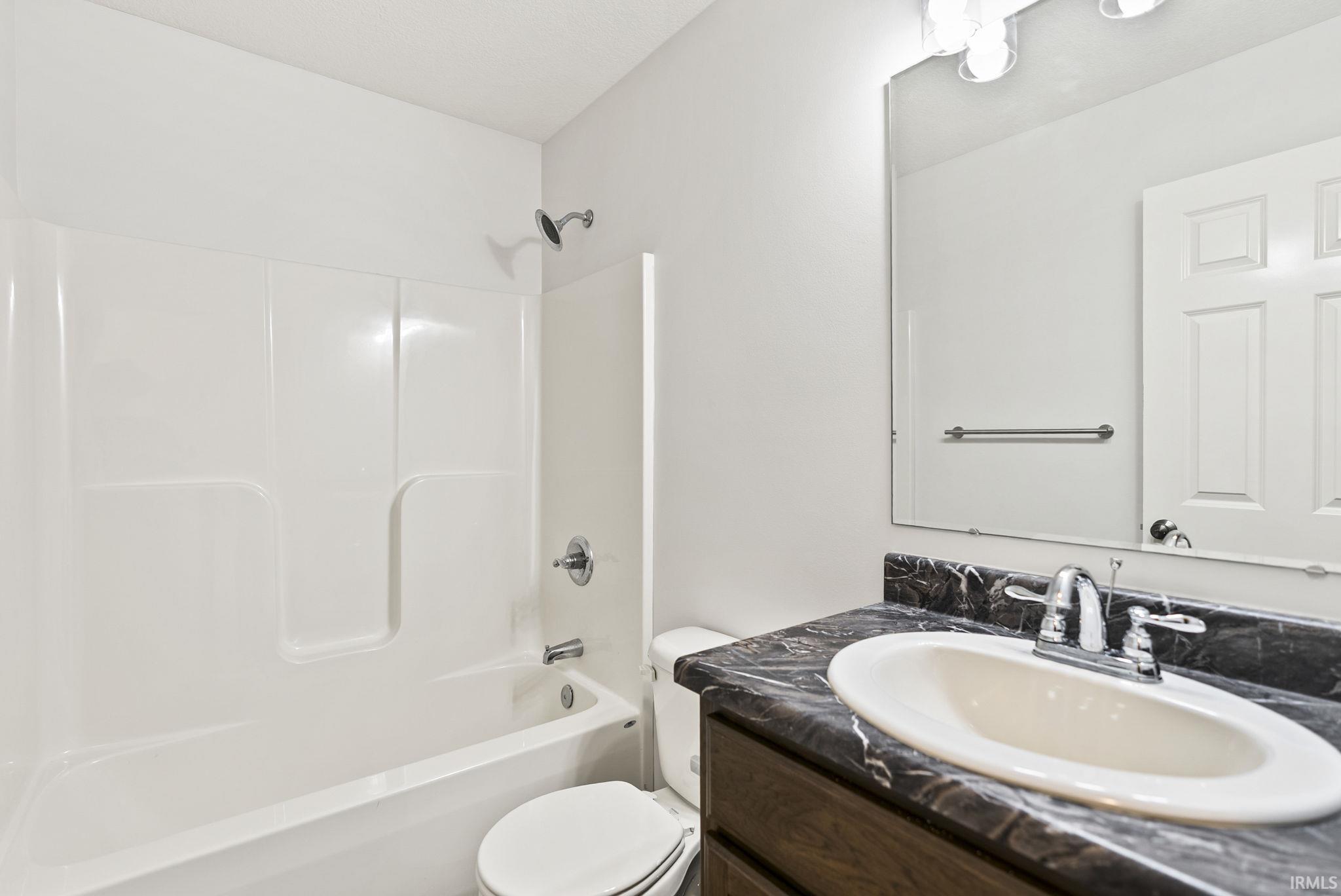 Bathroom featuring a white tub/shower combination, a dark wood-finish vanity with an integrated sink, a dark patterned countertop, and a large wall-mounted mirror