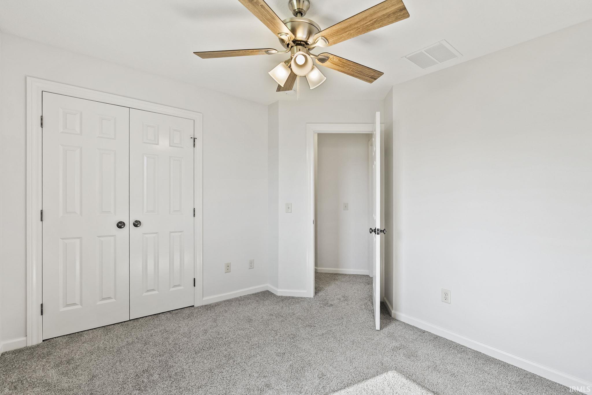 Room featuring light gray carpet, white walls, and a ceiling fan with wood-finish blades