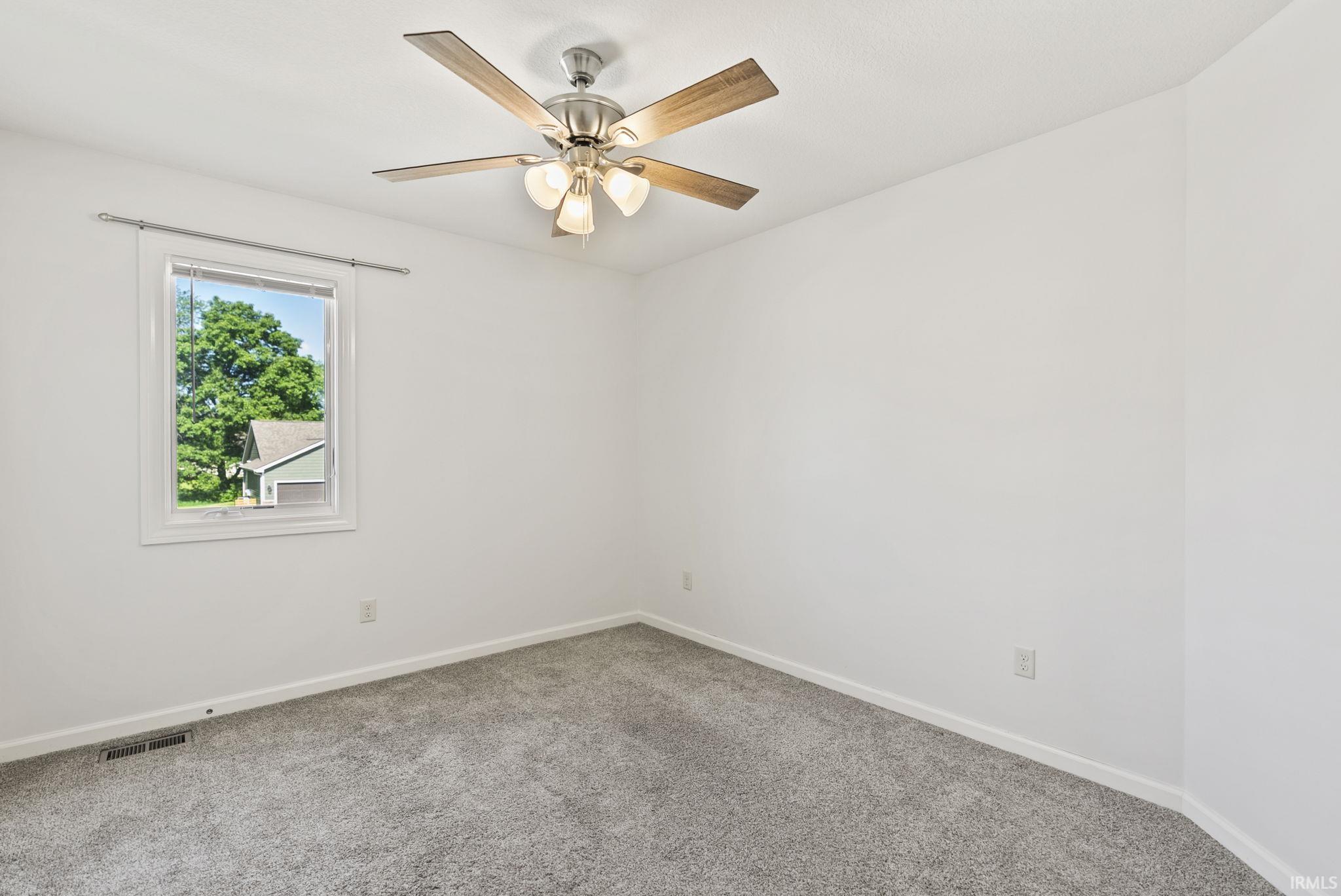Neutral white walls, grey carpet flooring, and a ceiling fan with light fixture