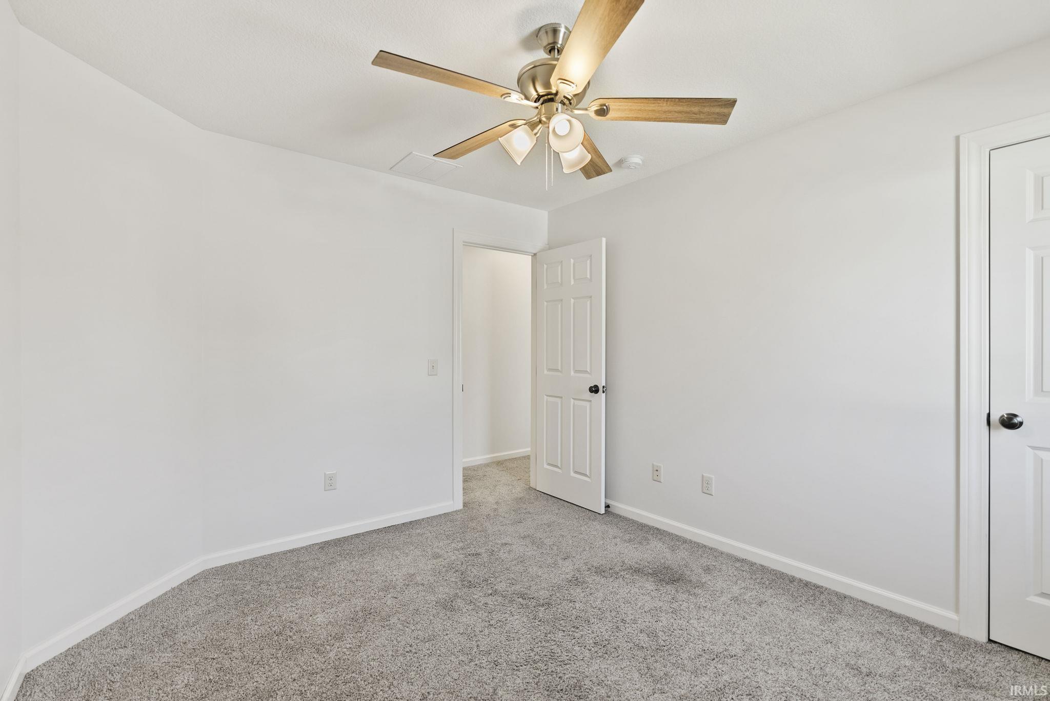 Carpeted room with white walls, a ceiling fan with light kit, and a paneled door