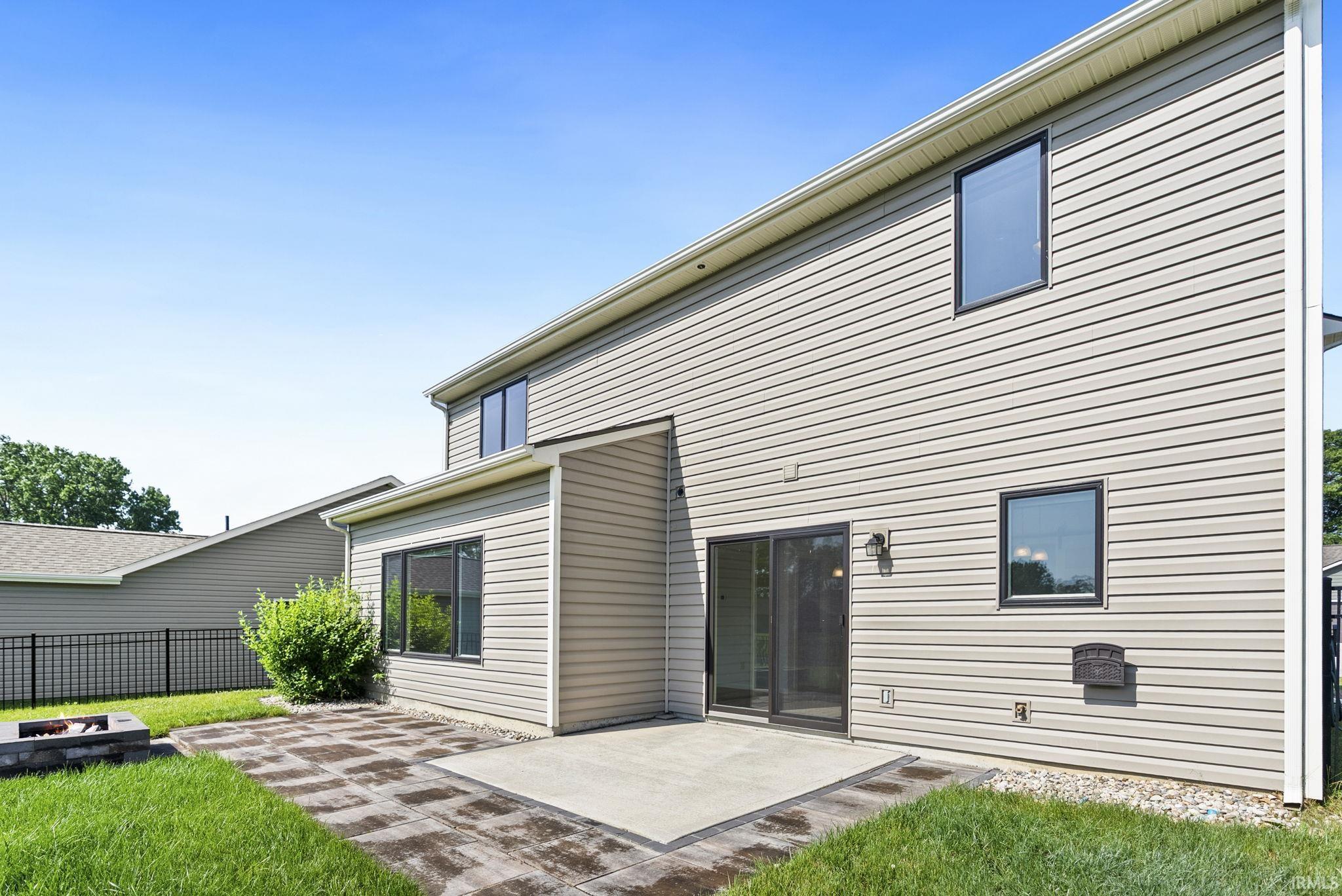 Two-story property with light-toned siding, featuring a concrete patio and paver stone patio
