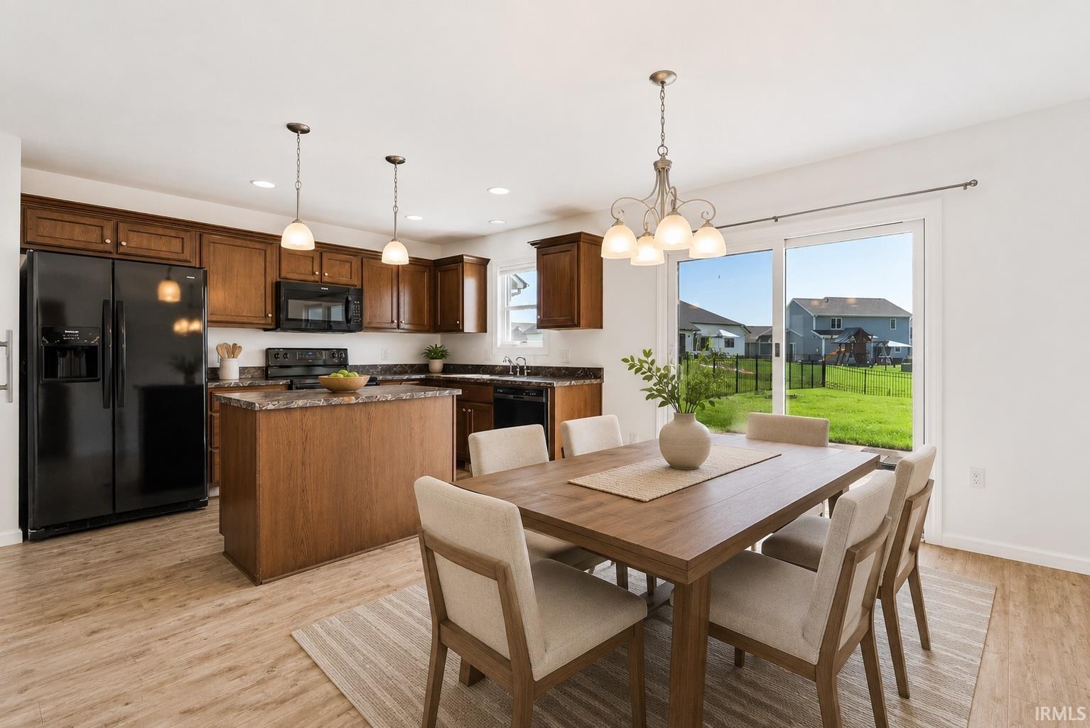 Open-concept kitchen and dining area featuring wood-finish flooring, dark wood cabinetry, a central kitchen island, and a sliding glass door