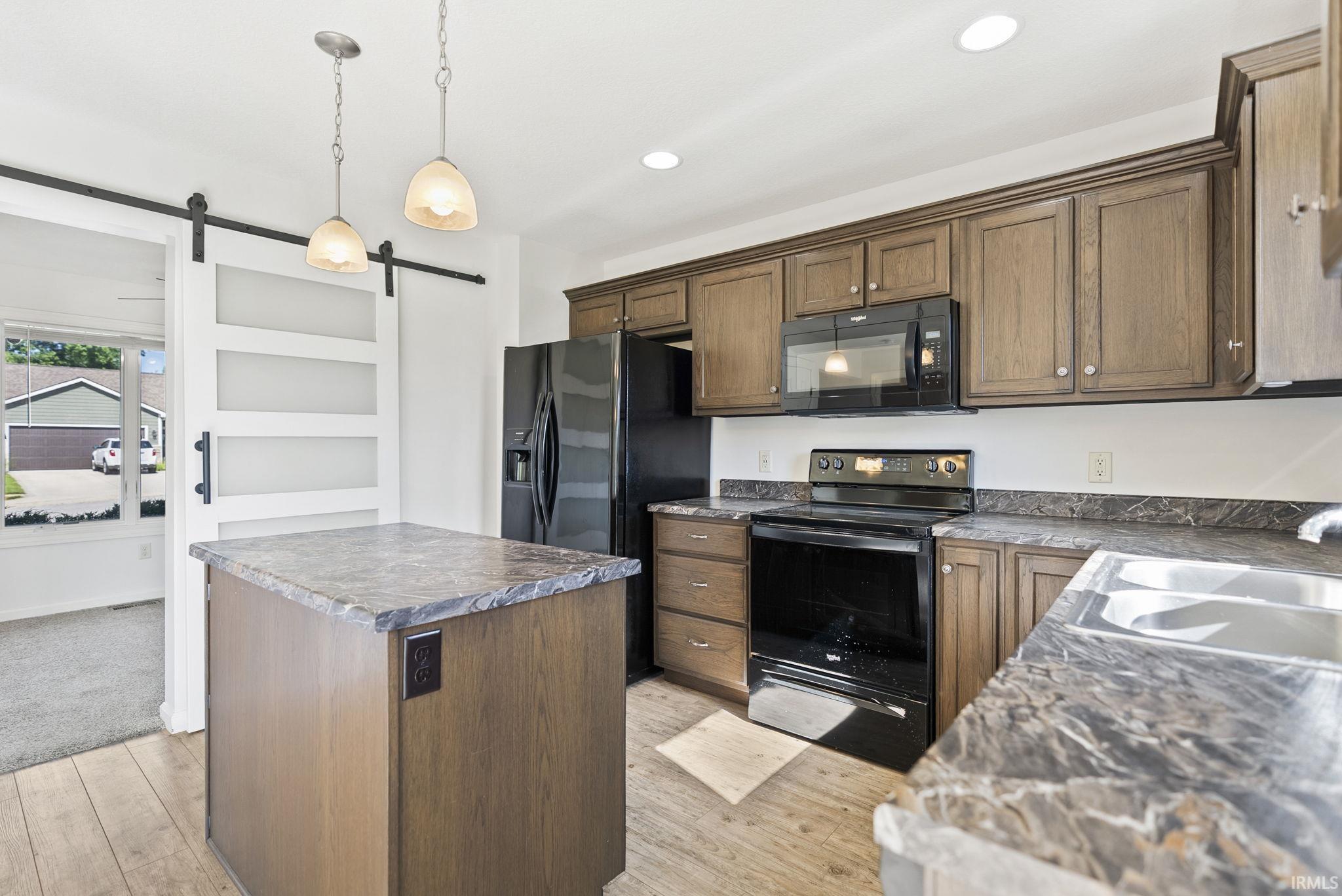 Kitchen featuring wood-finish cabinetry, black appliances, and stone-look countertops