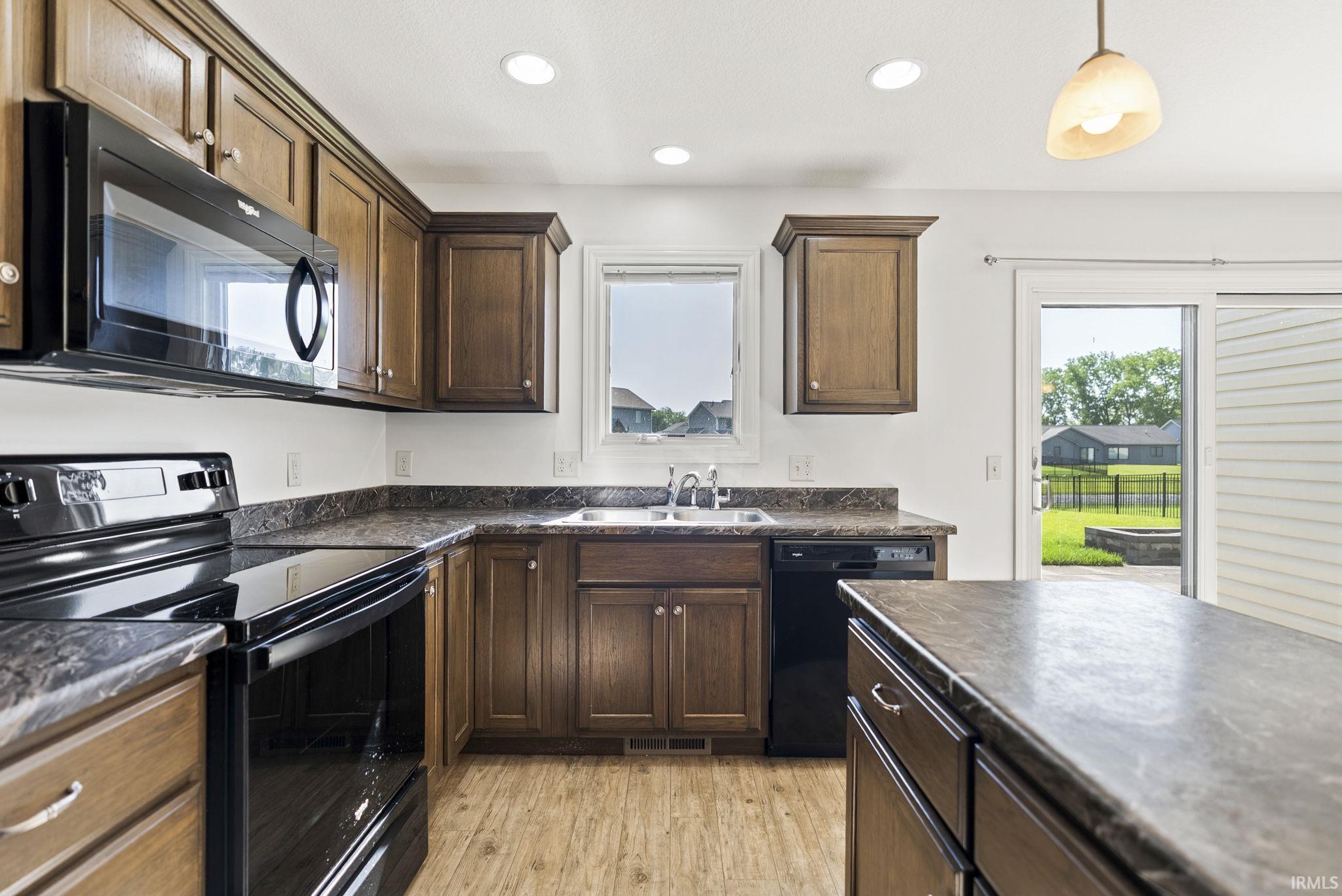 Kitchen featuring wood-finish cabinetry, dark countertops, black appliances, a double basin sink, and recessed lighting