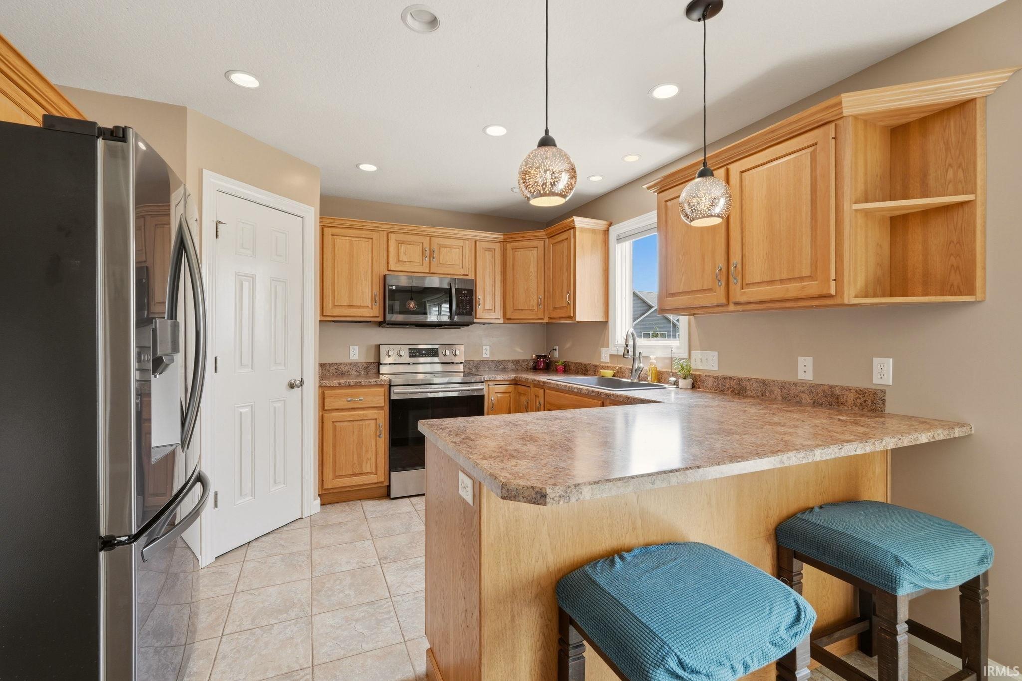 Kitchen featuring light wood cabinetry, a breakfast bar, recessed lighting, tile flooring, and stainless steel appliances